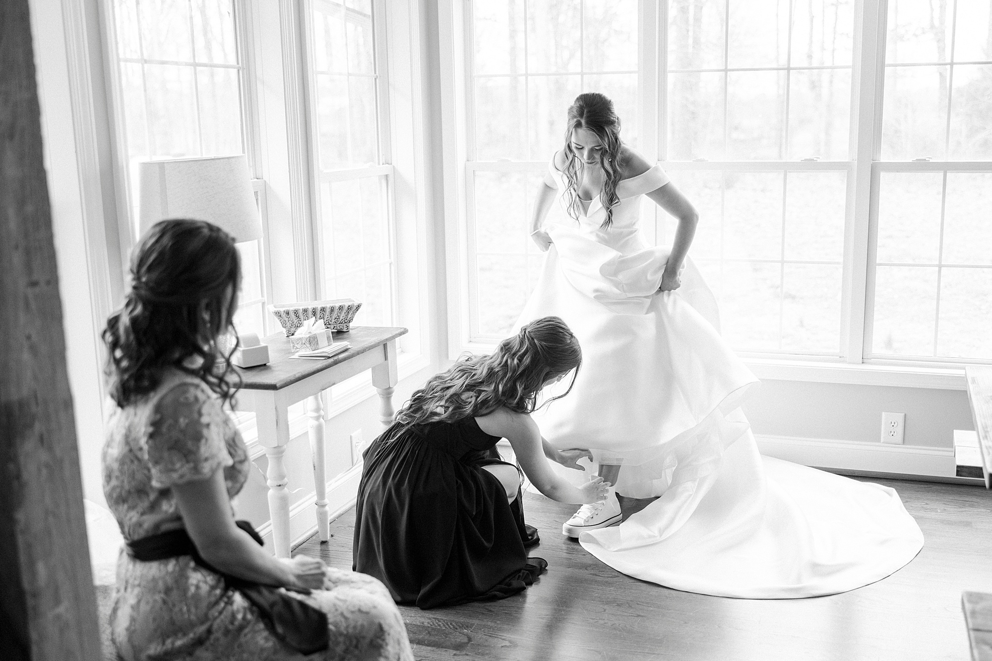 bridesmaid helps bride into shoes on wedding day