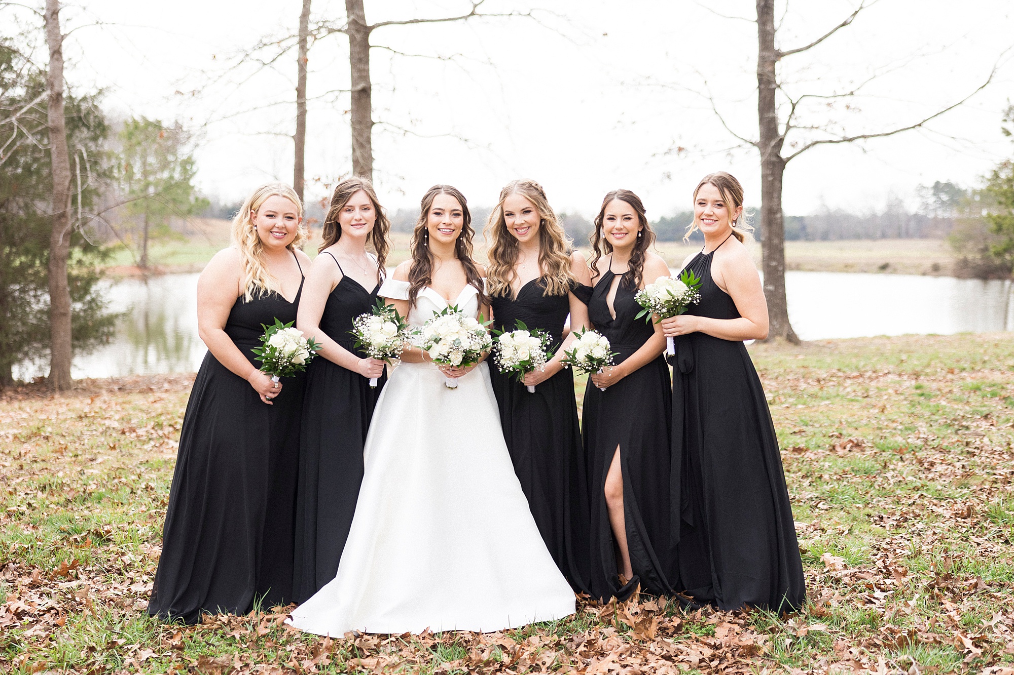 bridesmaids in mismatched black gowns pose with bride for winter wedding