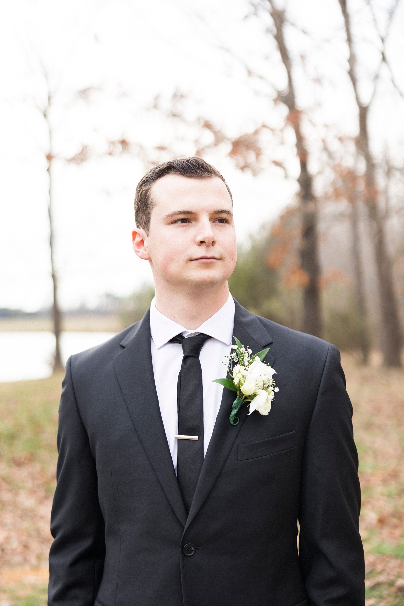 groom stands in woods in black suit