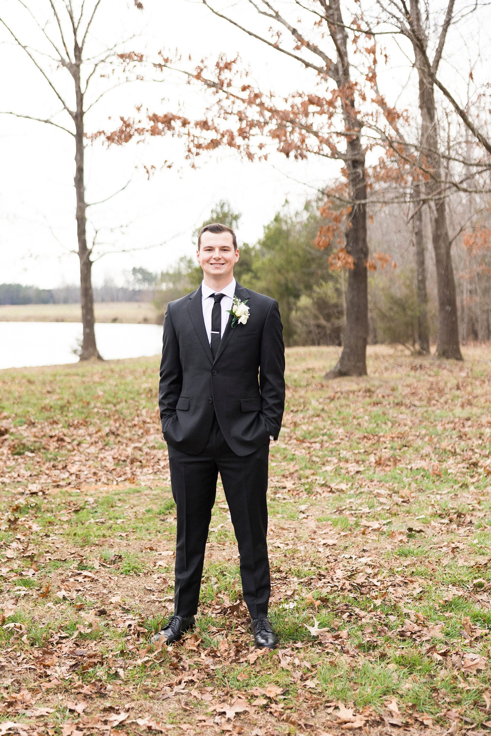 groom poses in black suit with white boutonnière