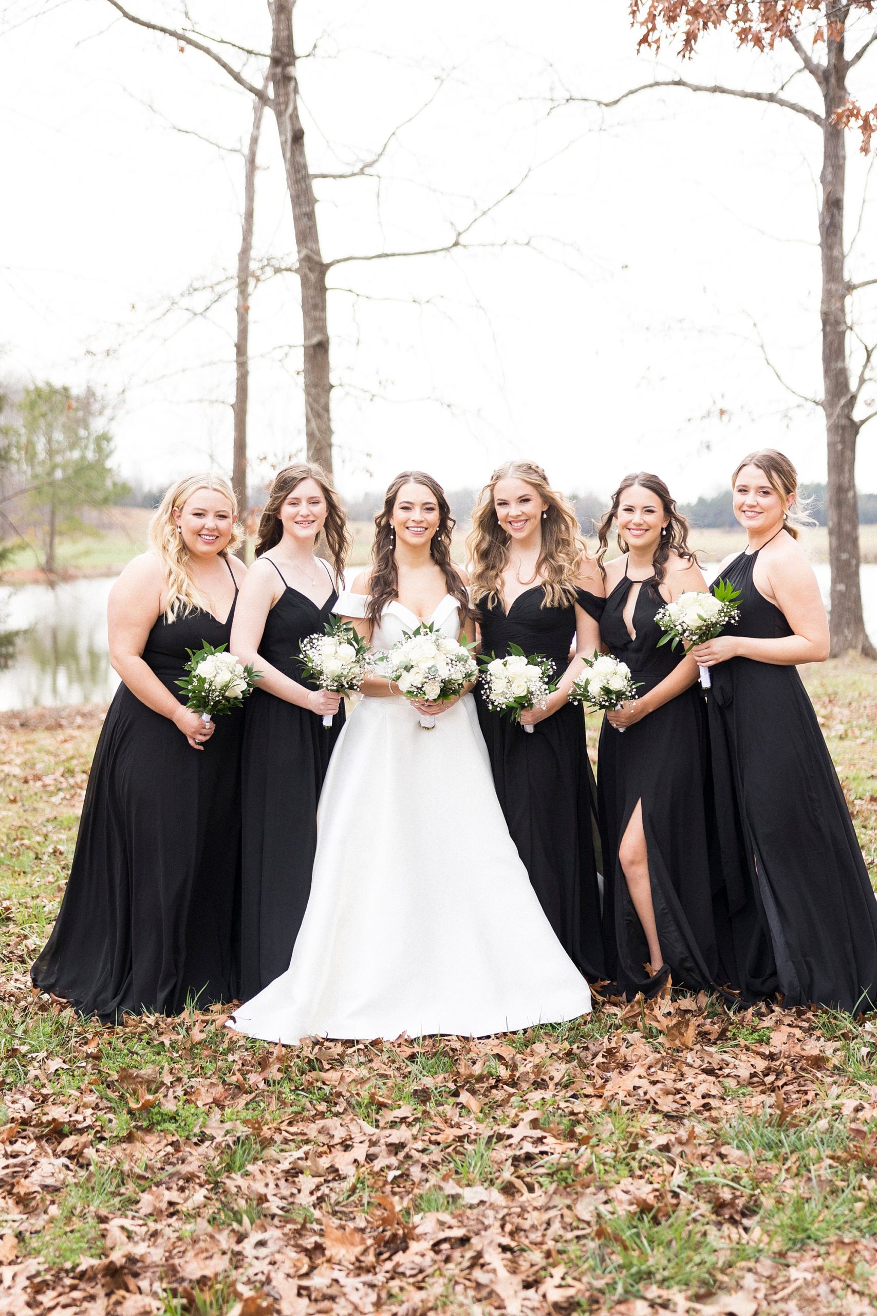 bride poses with bridesmaids in black gowns for winter wedding