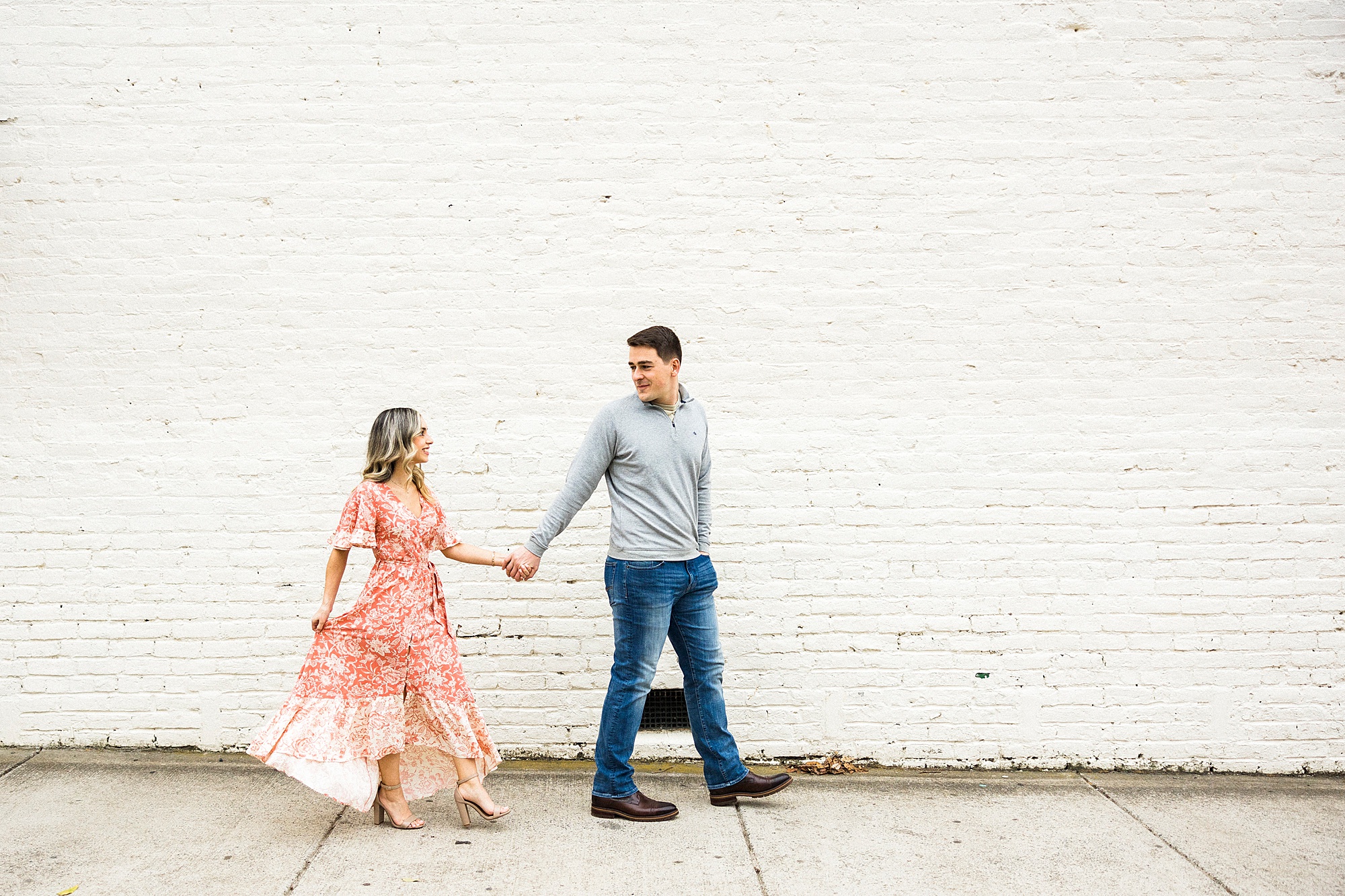 man leans woman against white wall during Downtown Concord engagement session