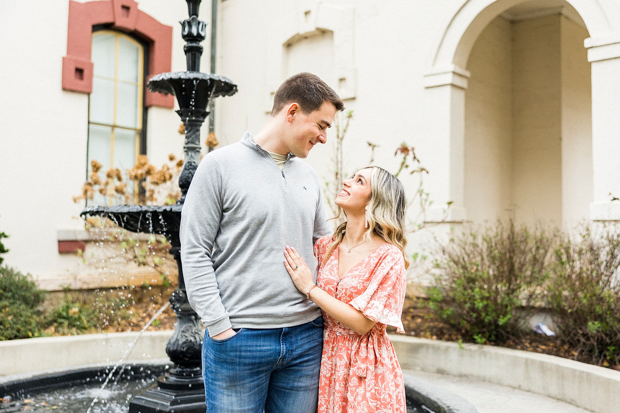 groom looks down at bride-to-be during engagement photos by fountain in downtown Concord