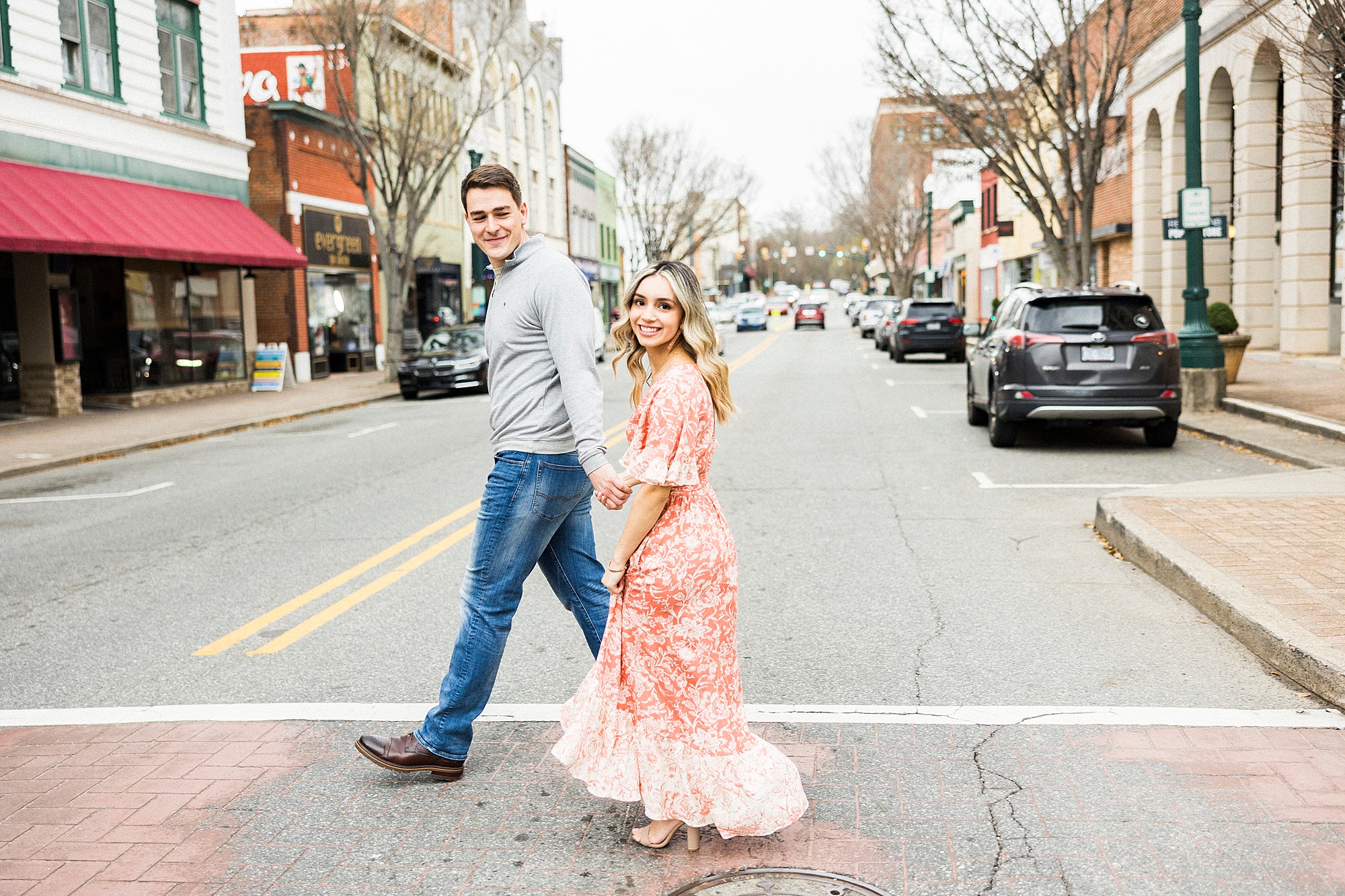 bride and groom hold hands walking through crosswalk during Downtown Concord engagement session