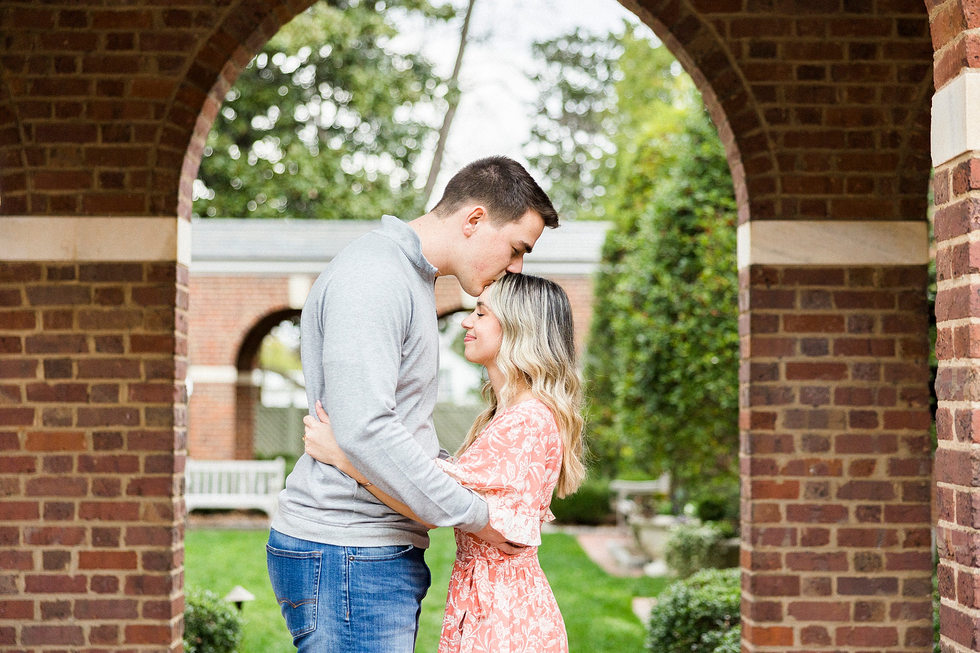 groom kisses fiancee's head during Downtown Concord engagement session under brick arch