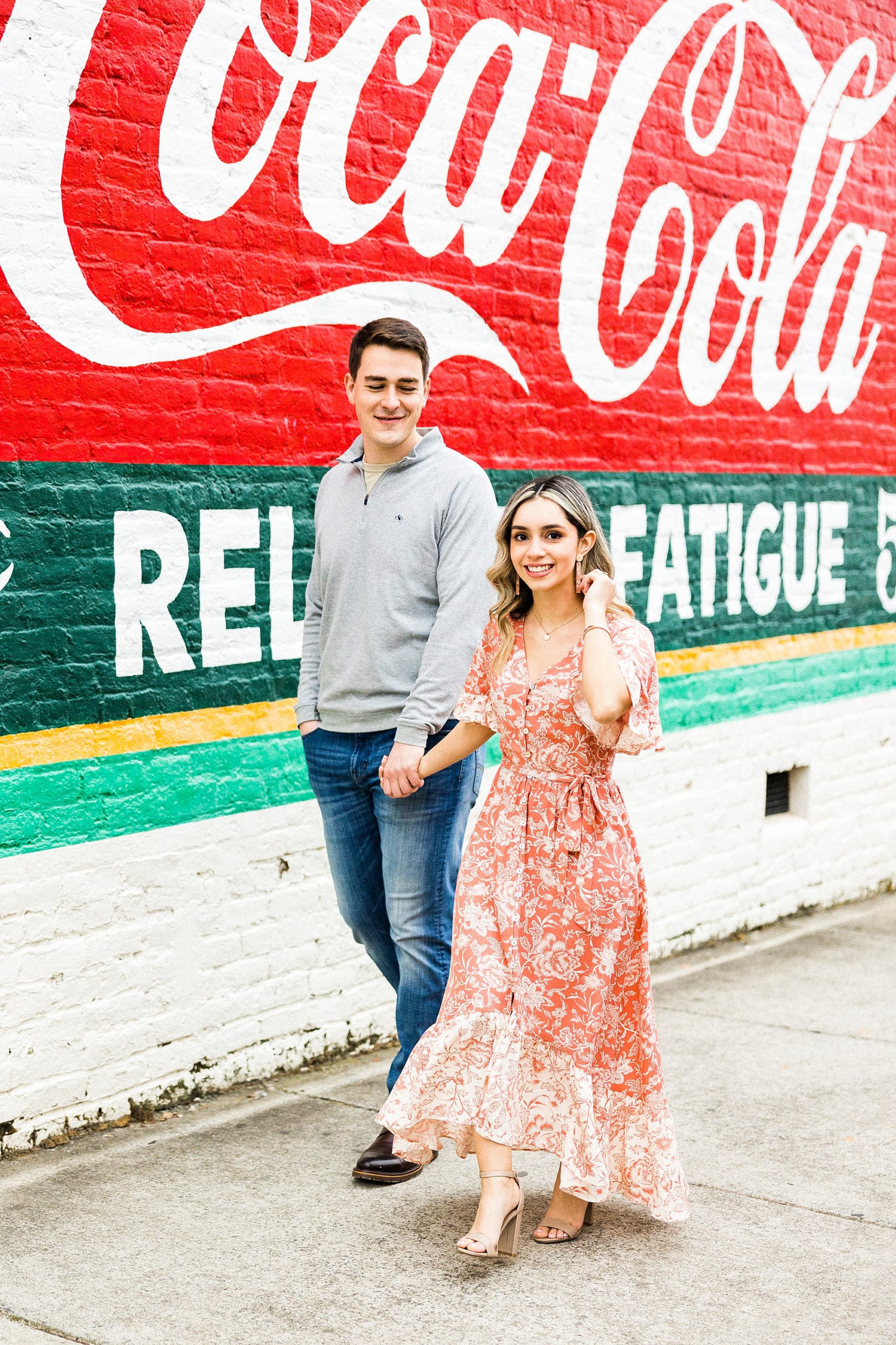 engaged couple walks by Coca-Cola mural during Downtown Concord engagement session
