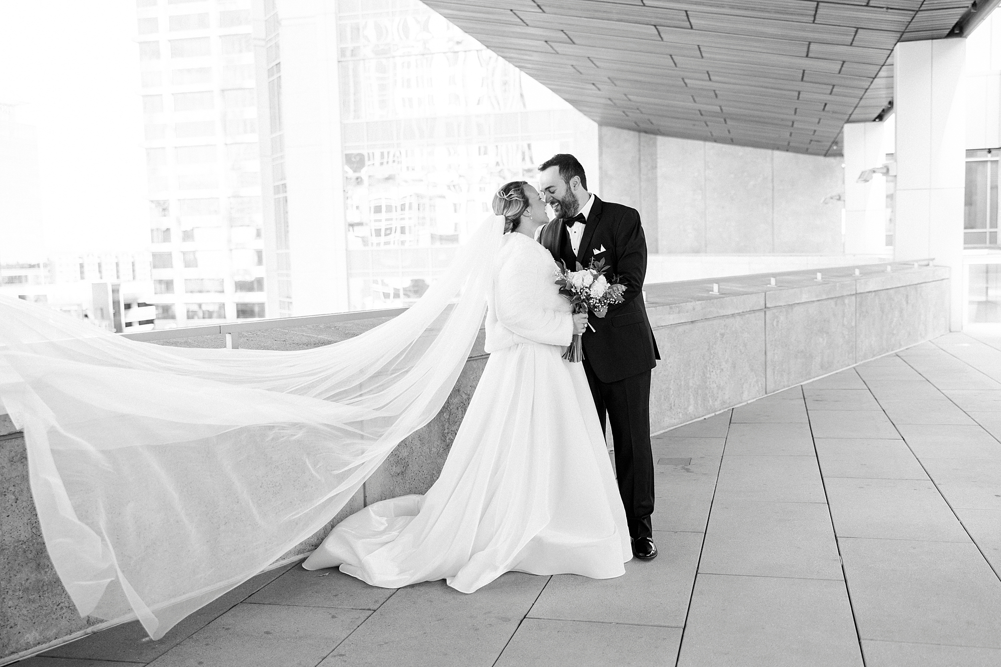 bride and groom kiss with veil floating behind them