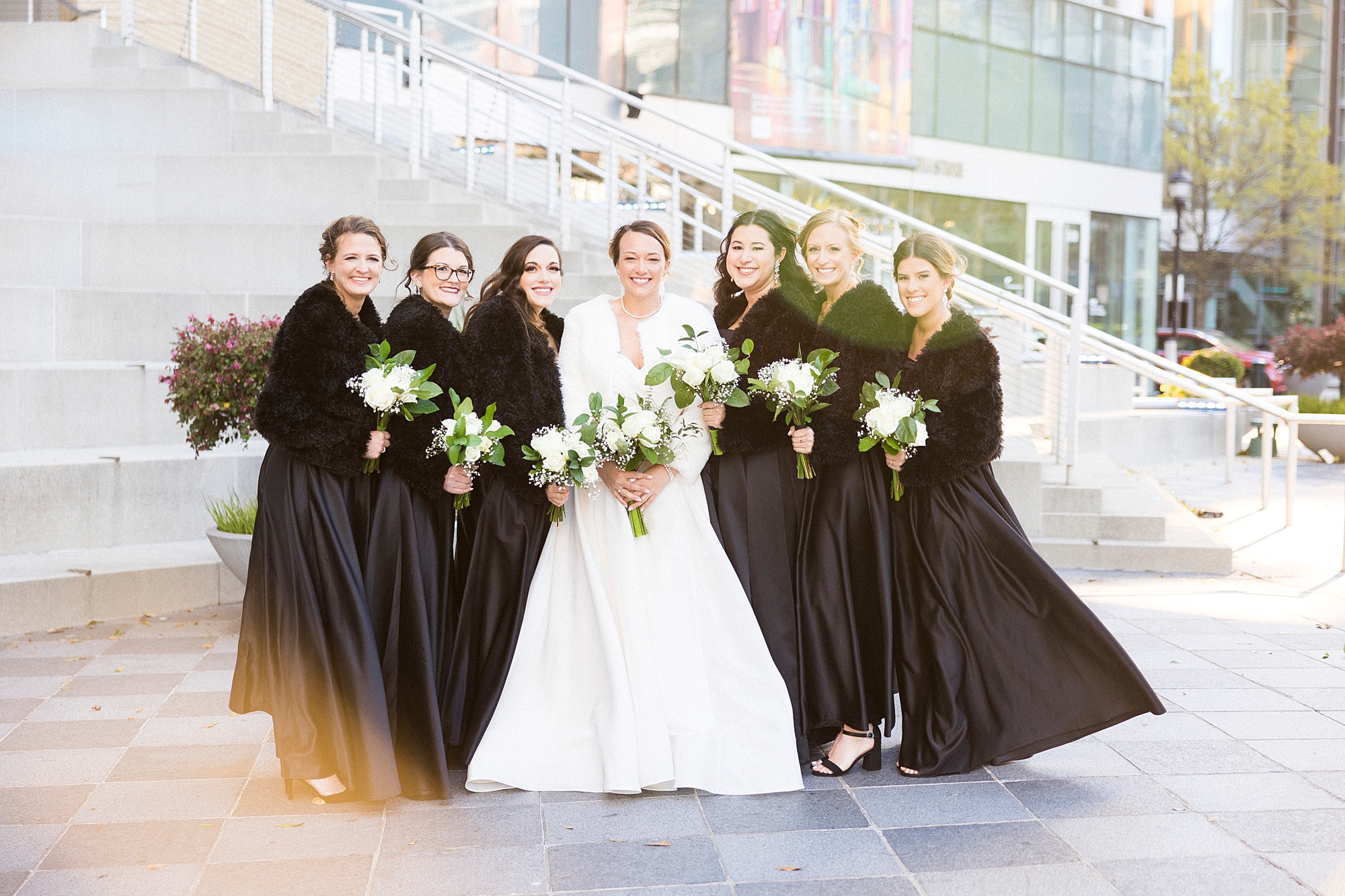bride poses with bridesmaids in black dresses with fur wraps