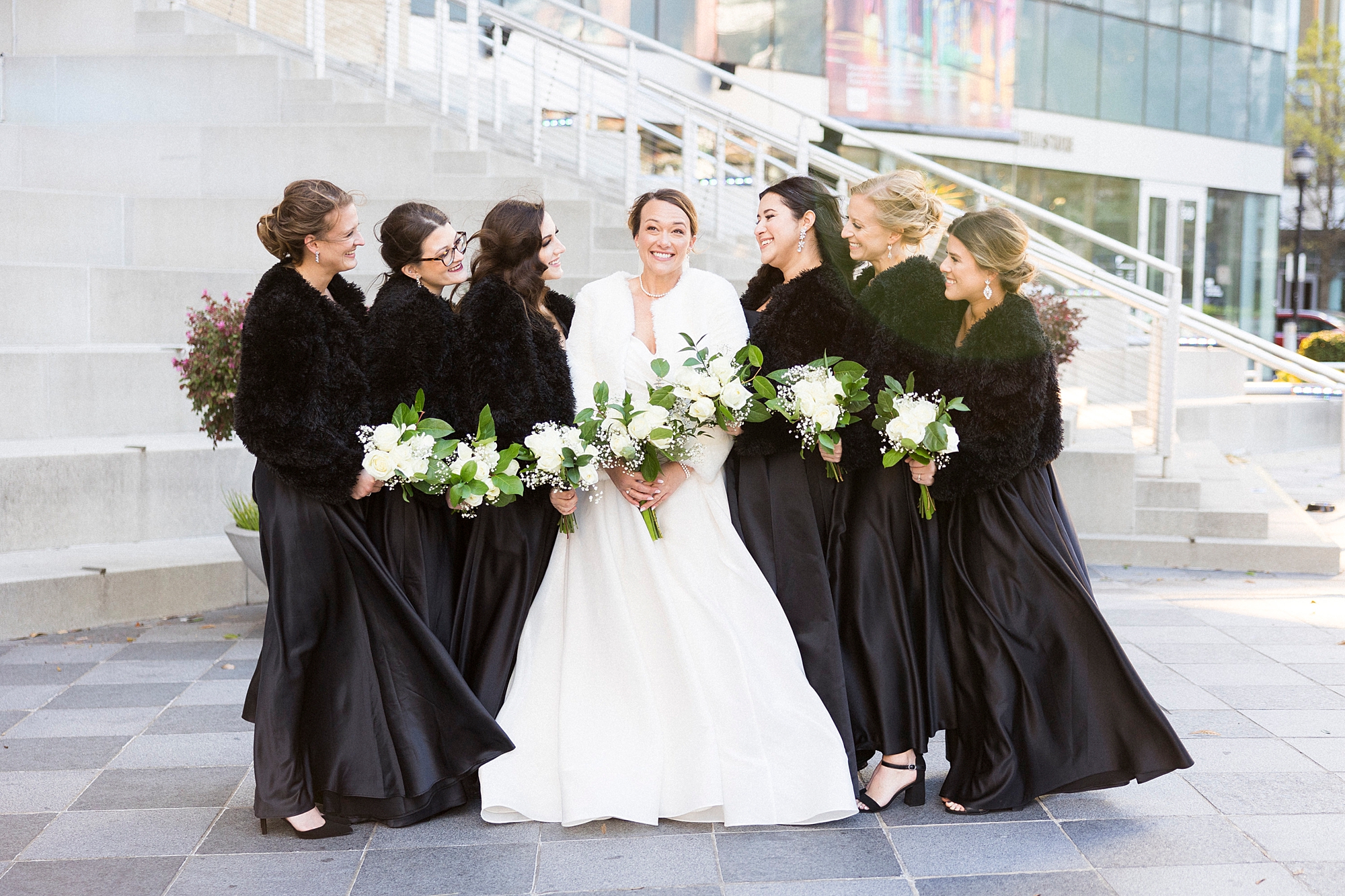 bride smiles with bridesmaids in black dresses and fur wraps