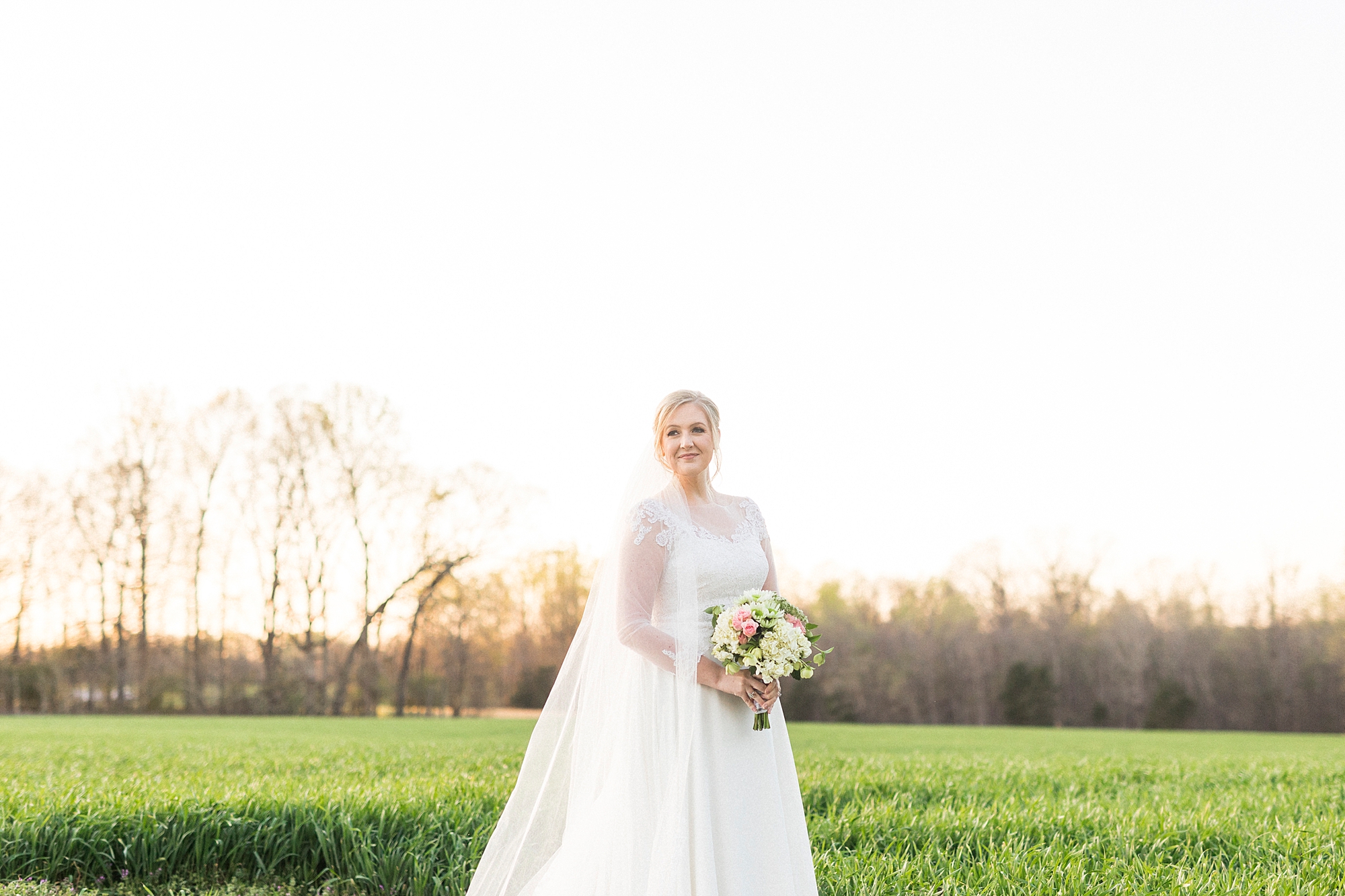 bride stands in field with veil draped behind her