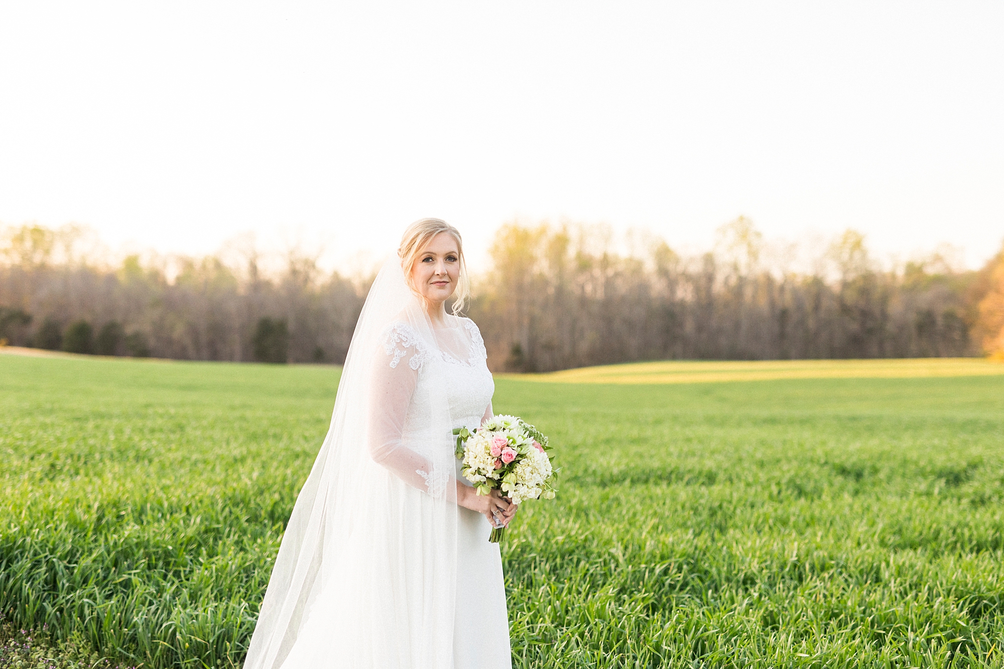 bride holds bouquet on edge of field in Mooresville NC