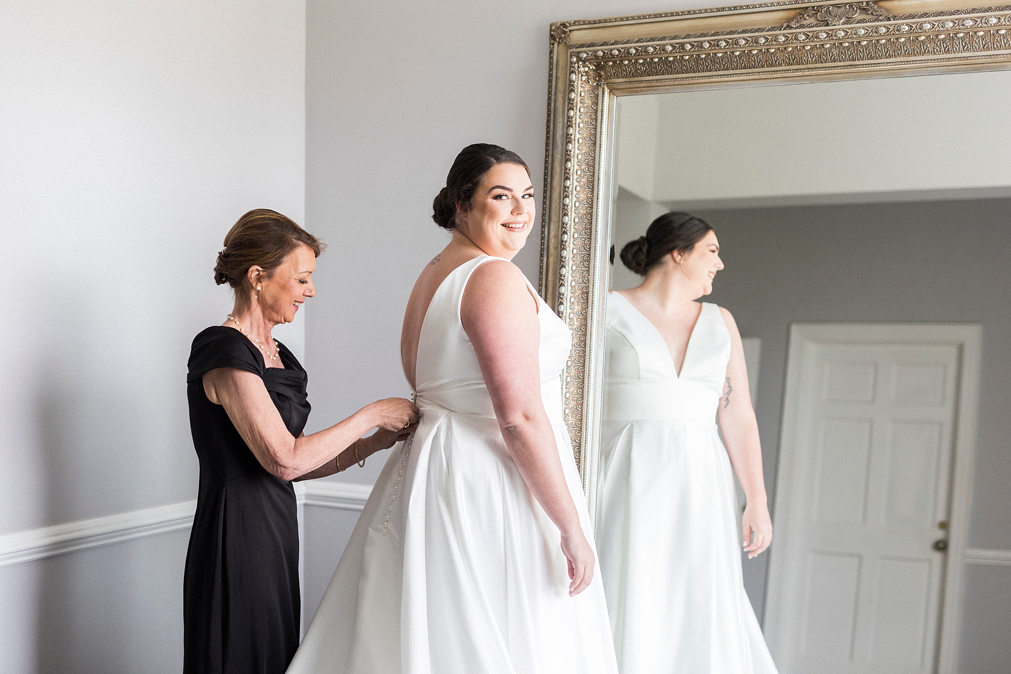 mom helps bride into wedding gown by mirror before spring Separk Mansion wedding ceremony