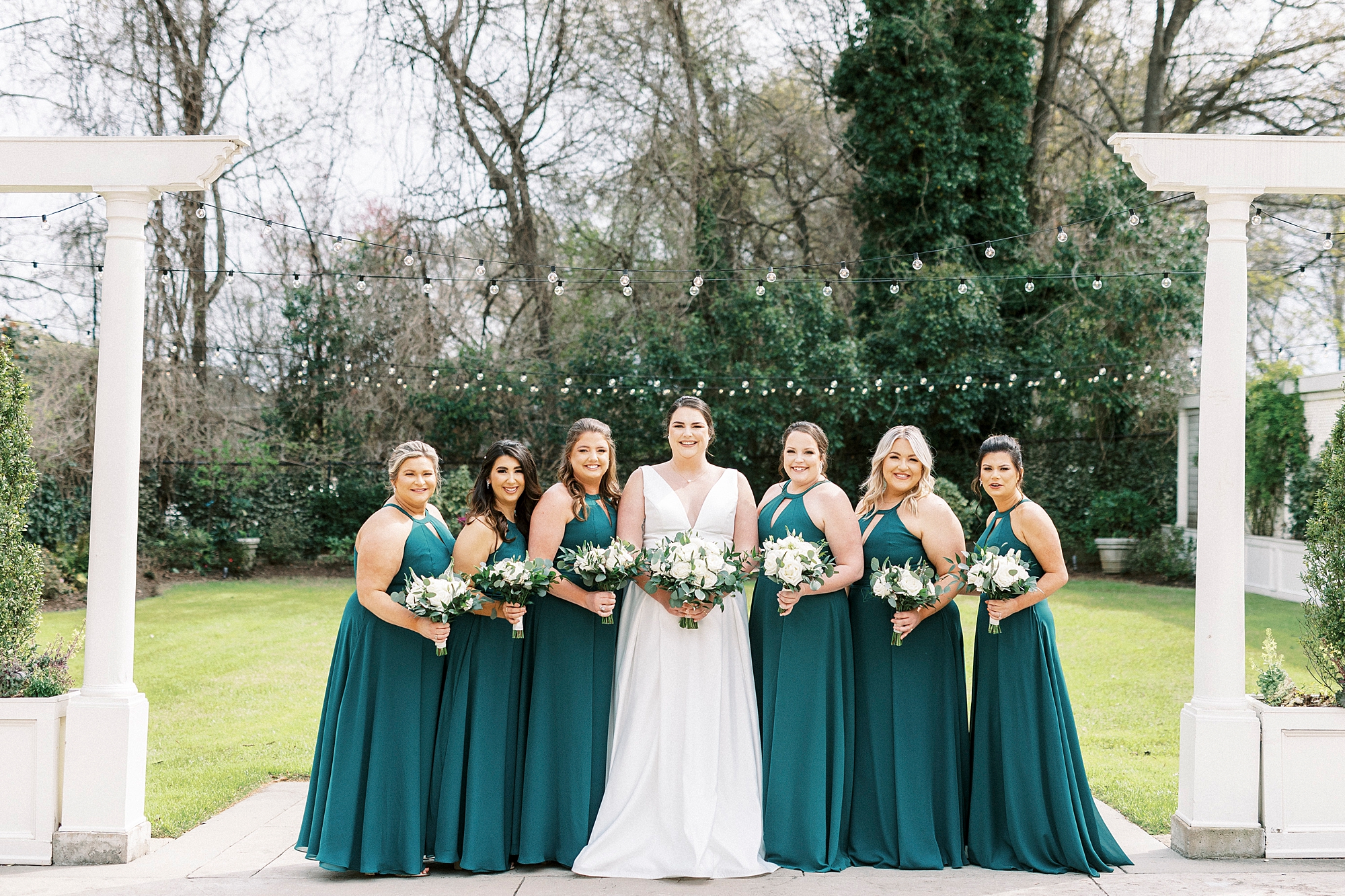 bride stands with bridesmaids in emerald green dresses