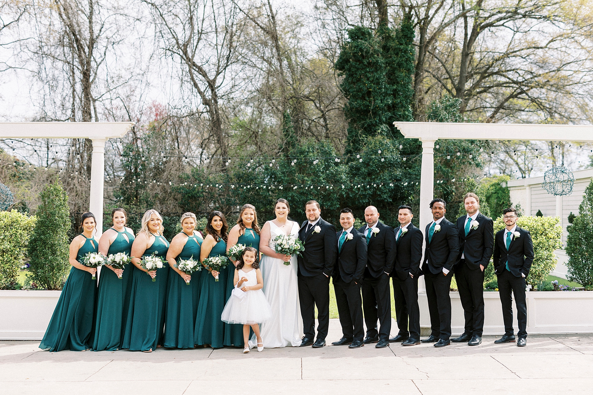 bride and groom stand with wedding party in emerald green gowns and black suits
