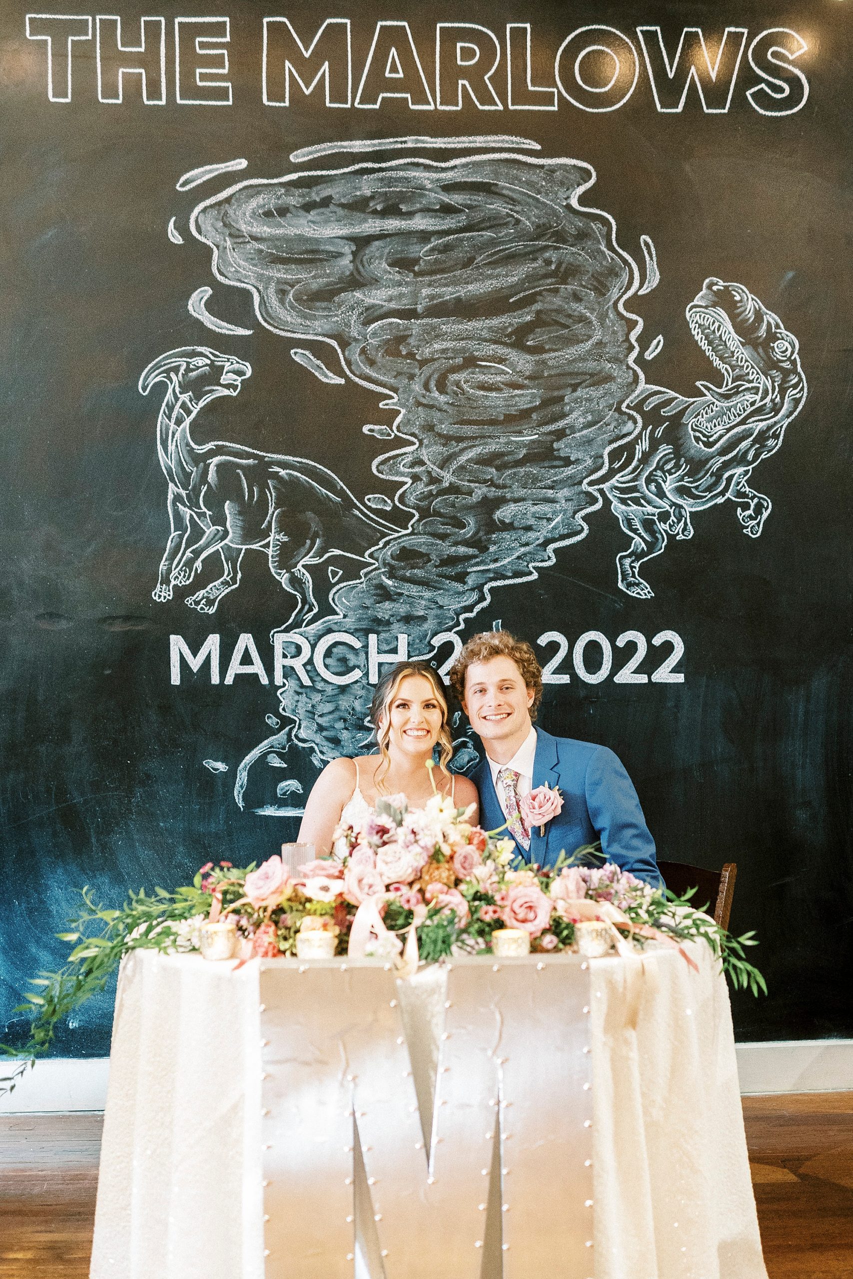 bride and groom sit at sweetheart table by chalkboard