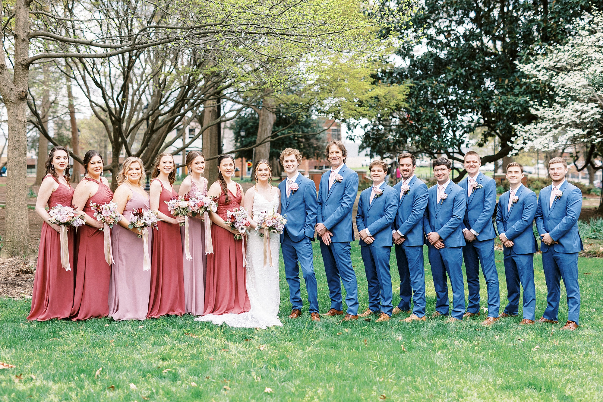 newlyweds stand with wedding party in pink and blue