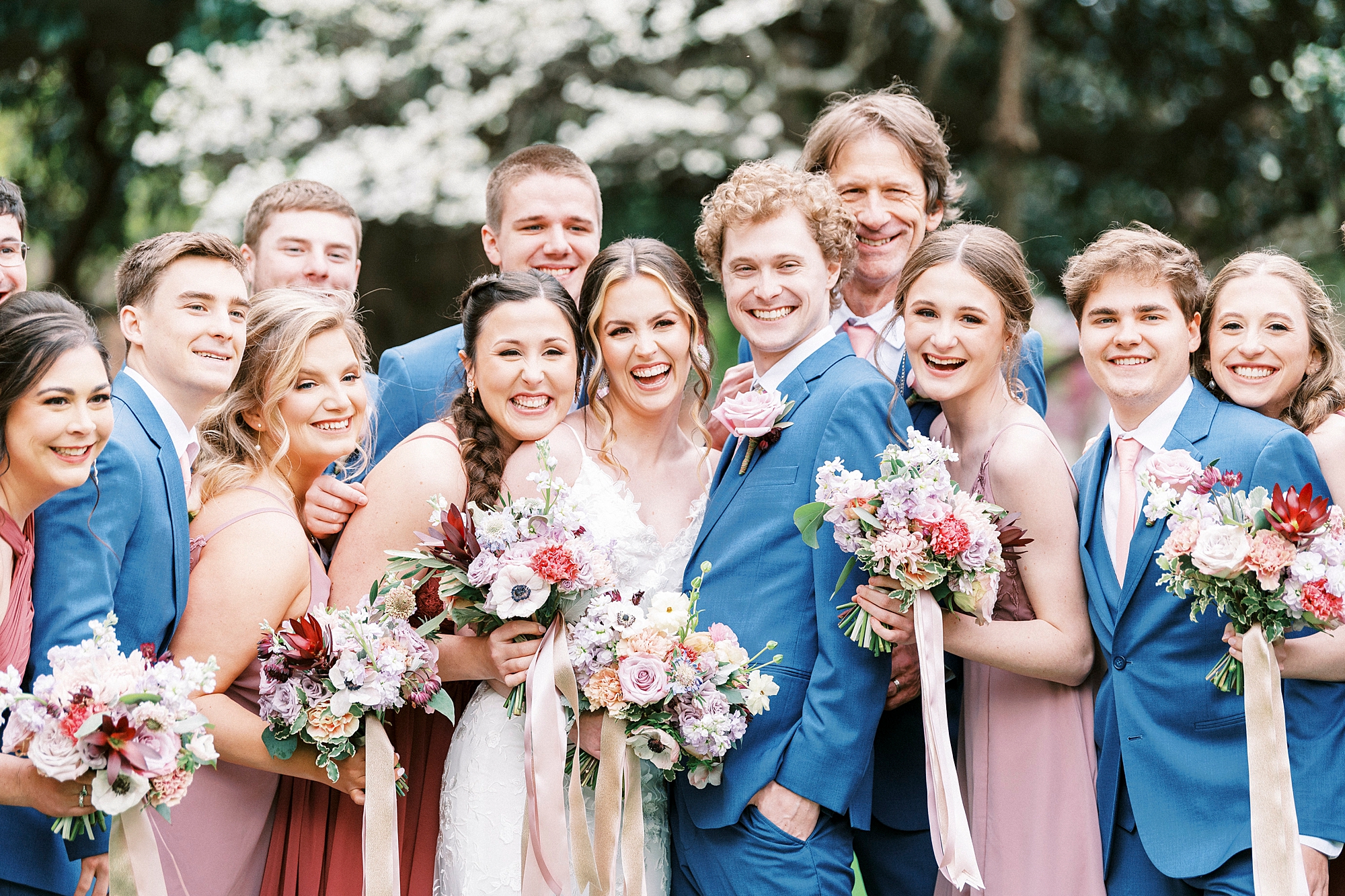 newlyweds hug together with wedding party in blue suits and pink dresses