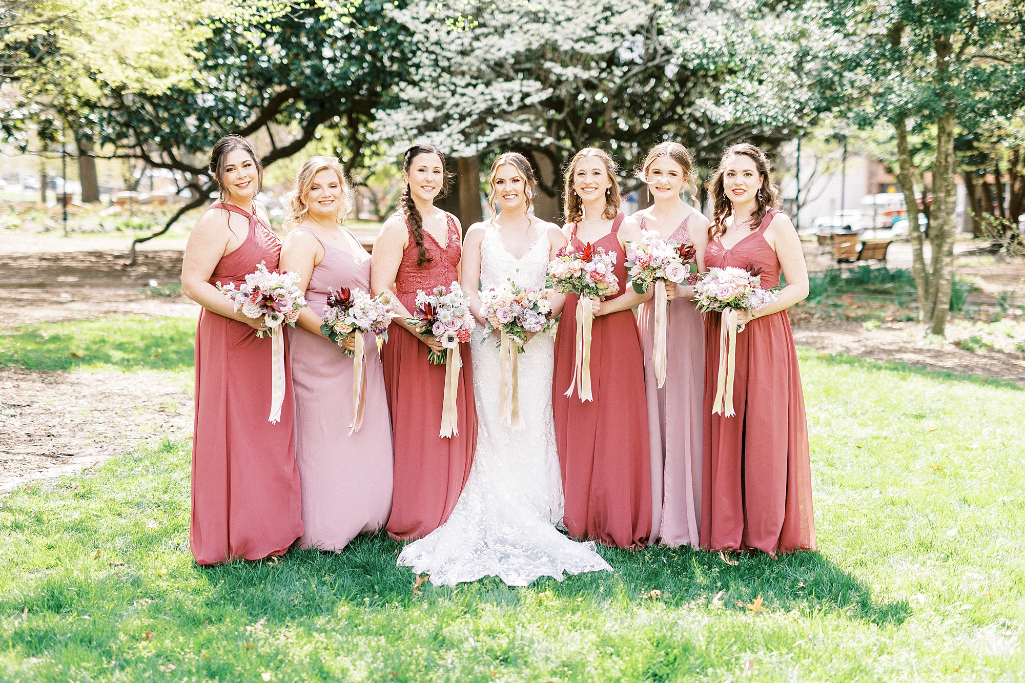 bride stands with bridesmaids in mismatched pink gowns