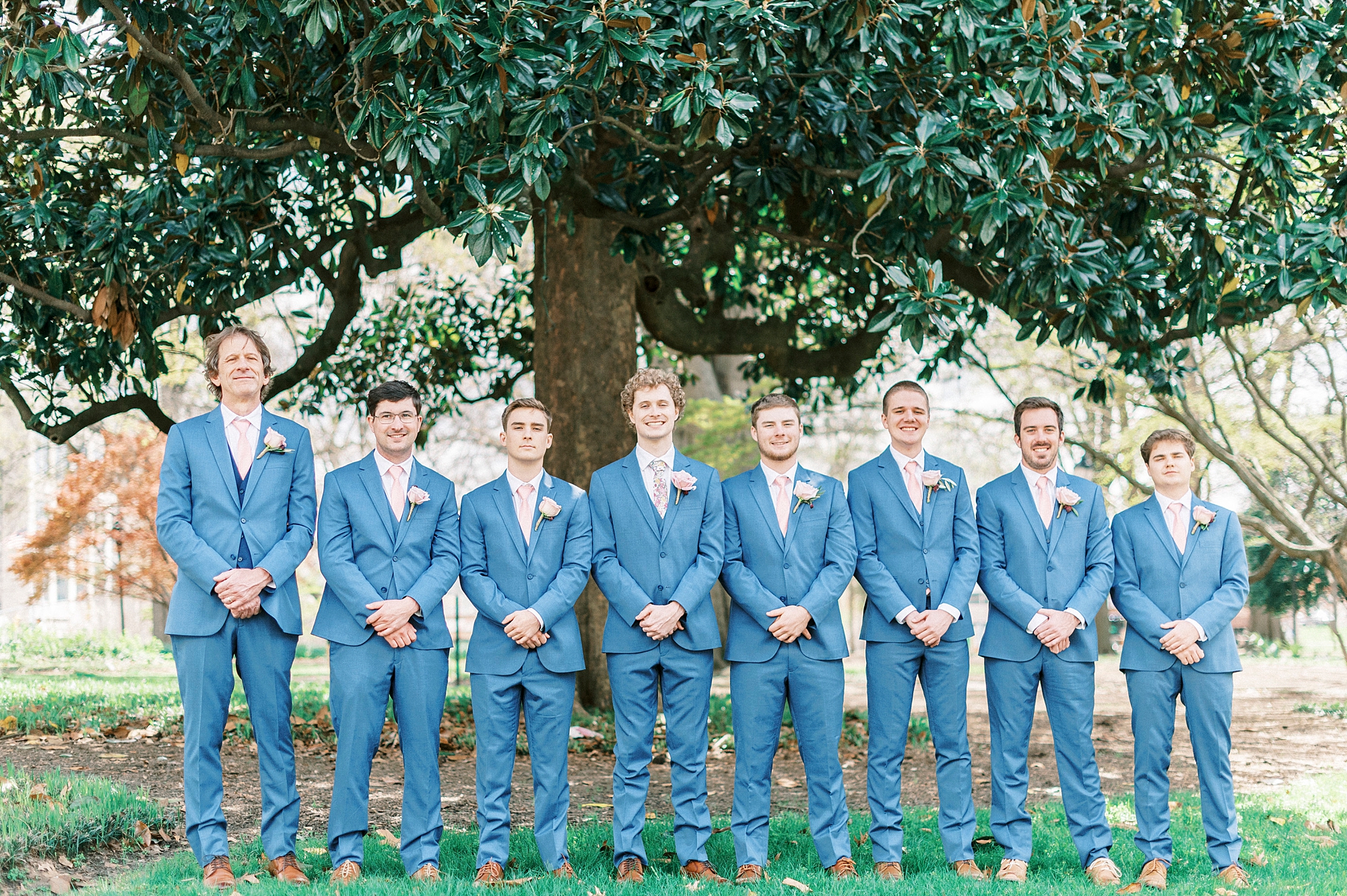 groom stands with groomsmen in blue suits