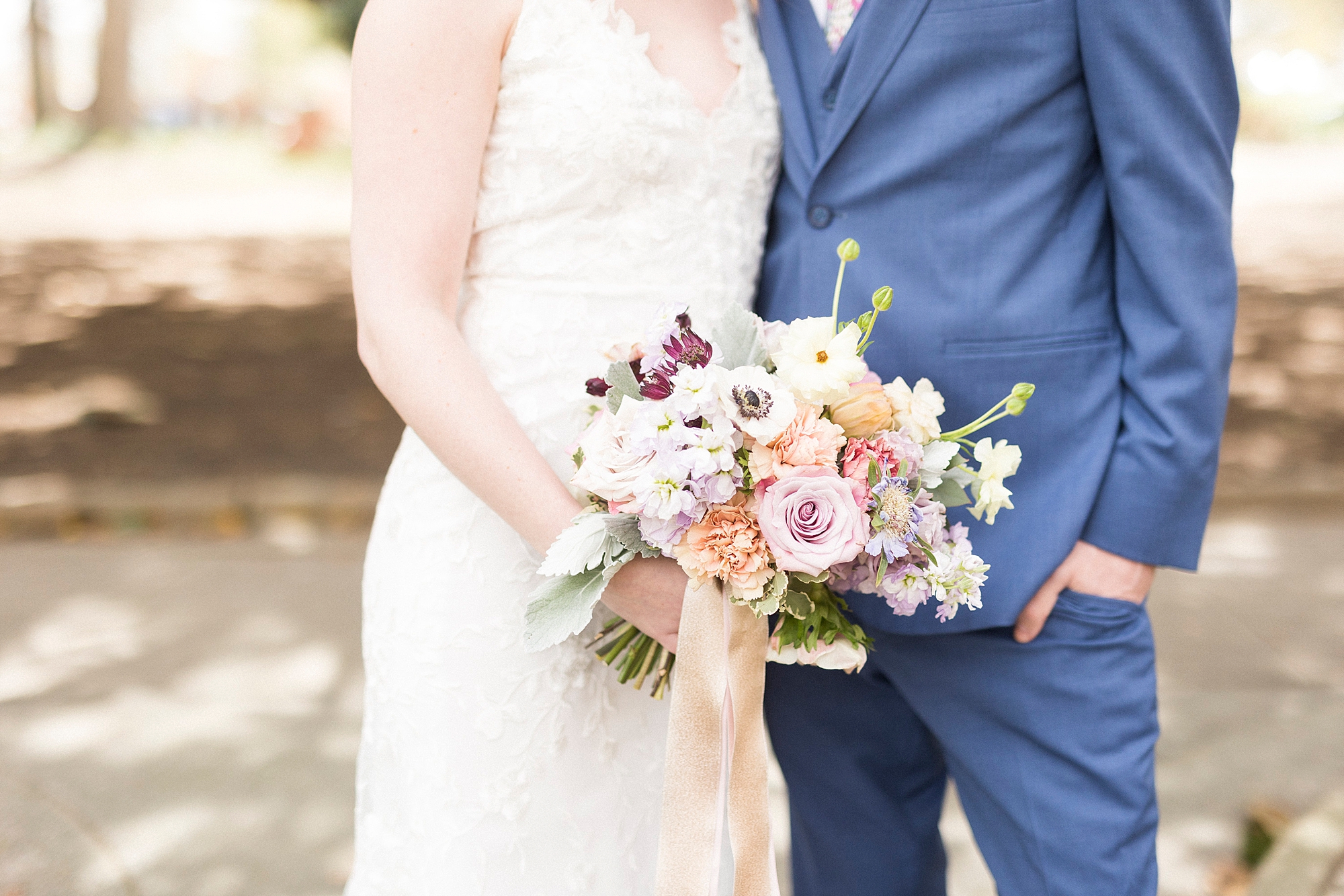 couple hugs during spring wedding portraits at Stockroom at 230 while bride holds pastel bouquet