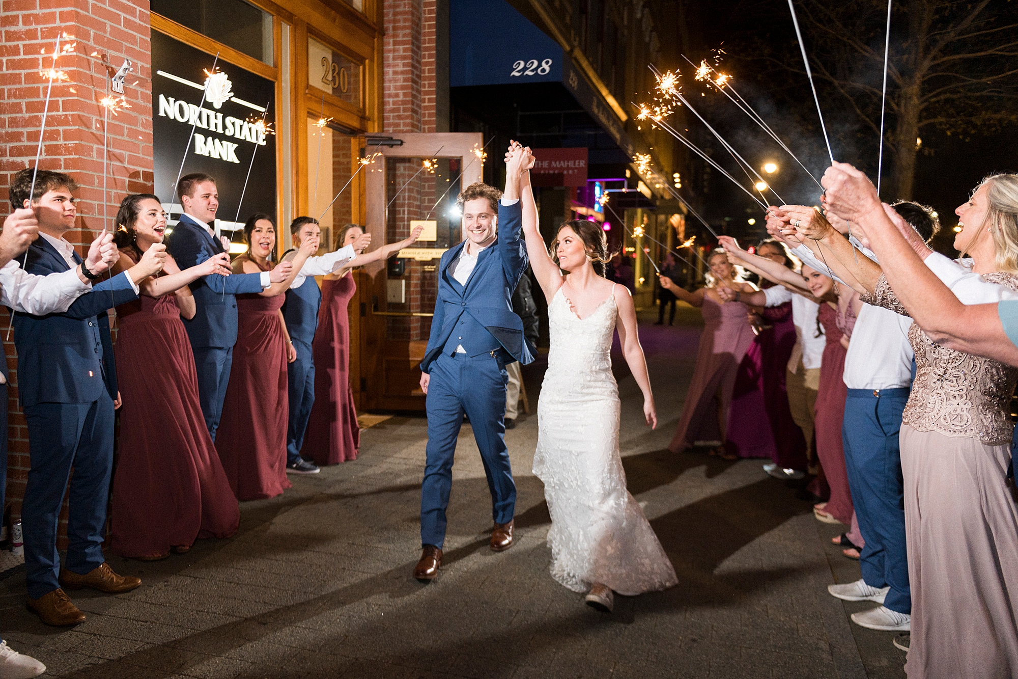 bride and groom hold hands walking though sparkler exit