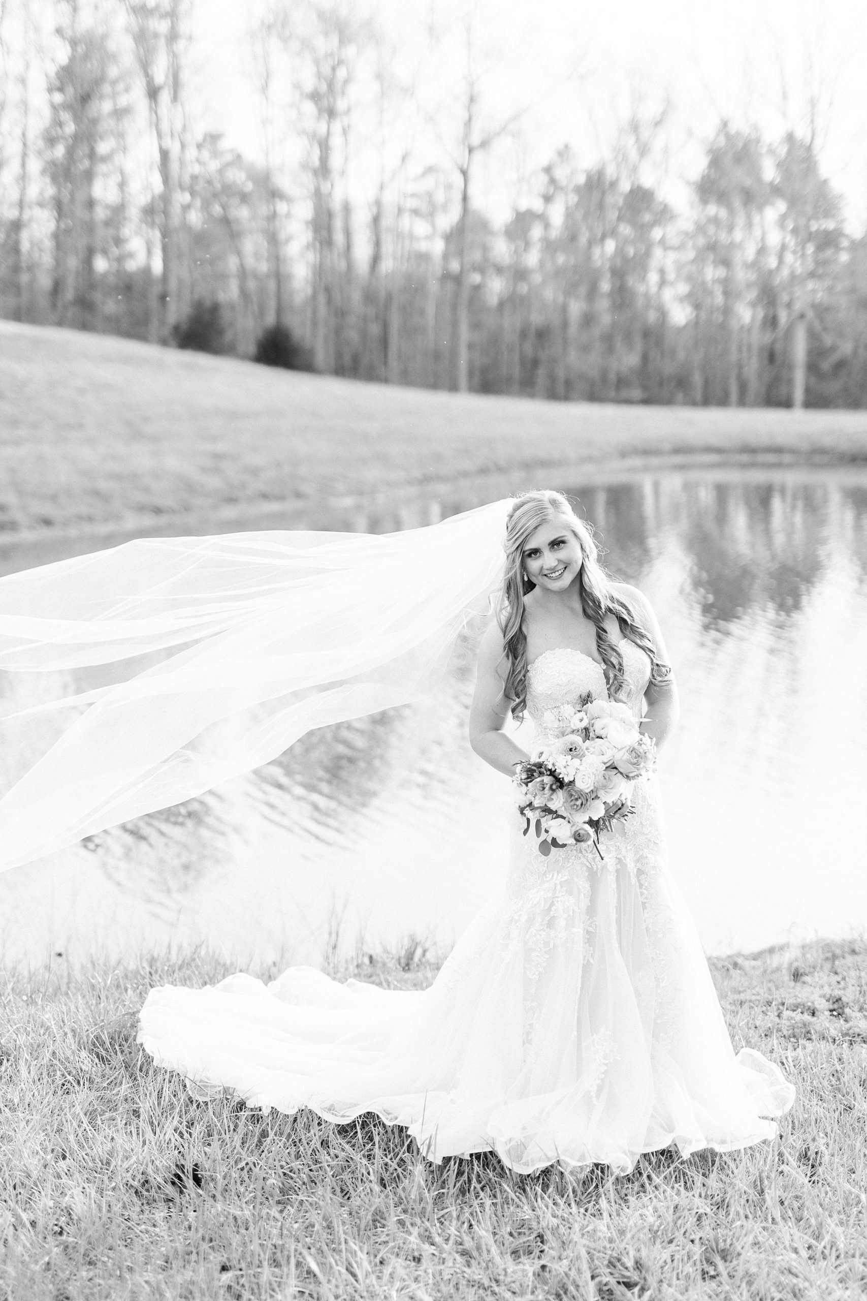 bride smiles standing by lake with veil floating