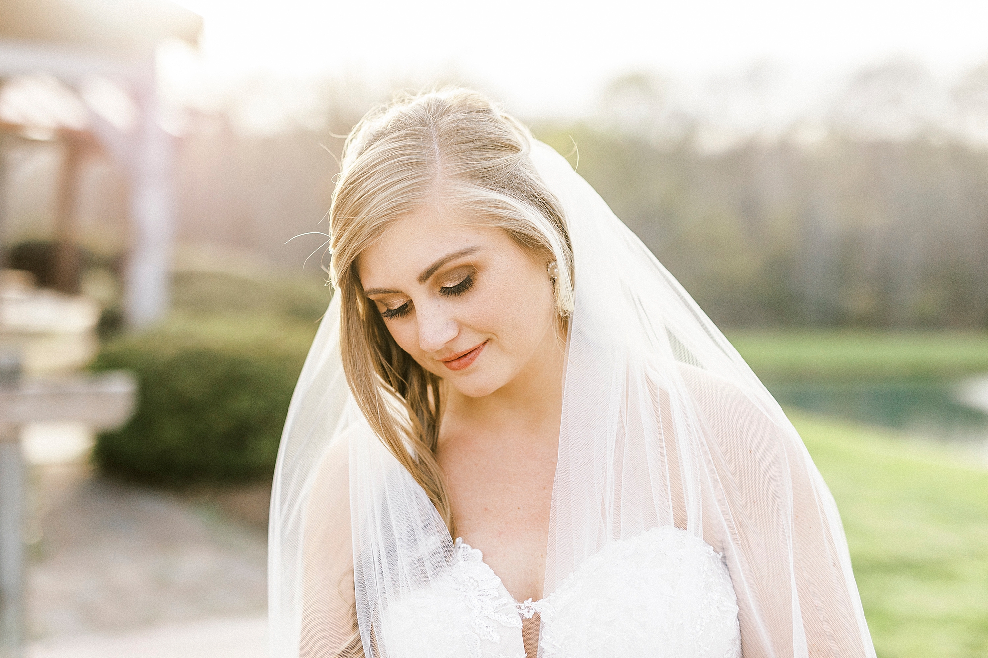 bride smiles down at hands with veil around shoulders 