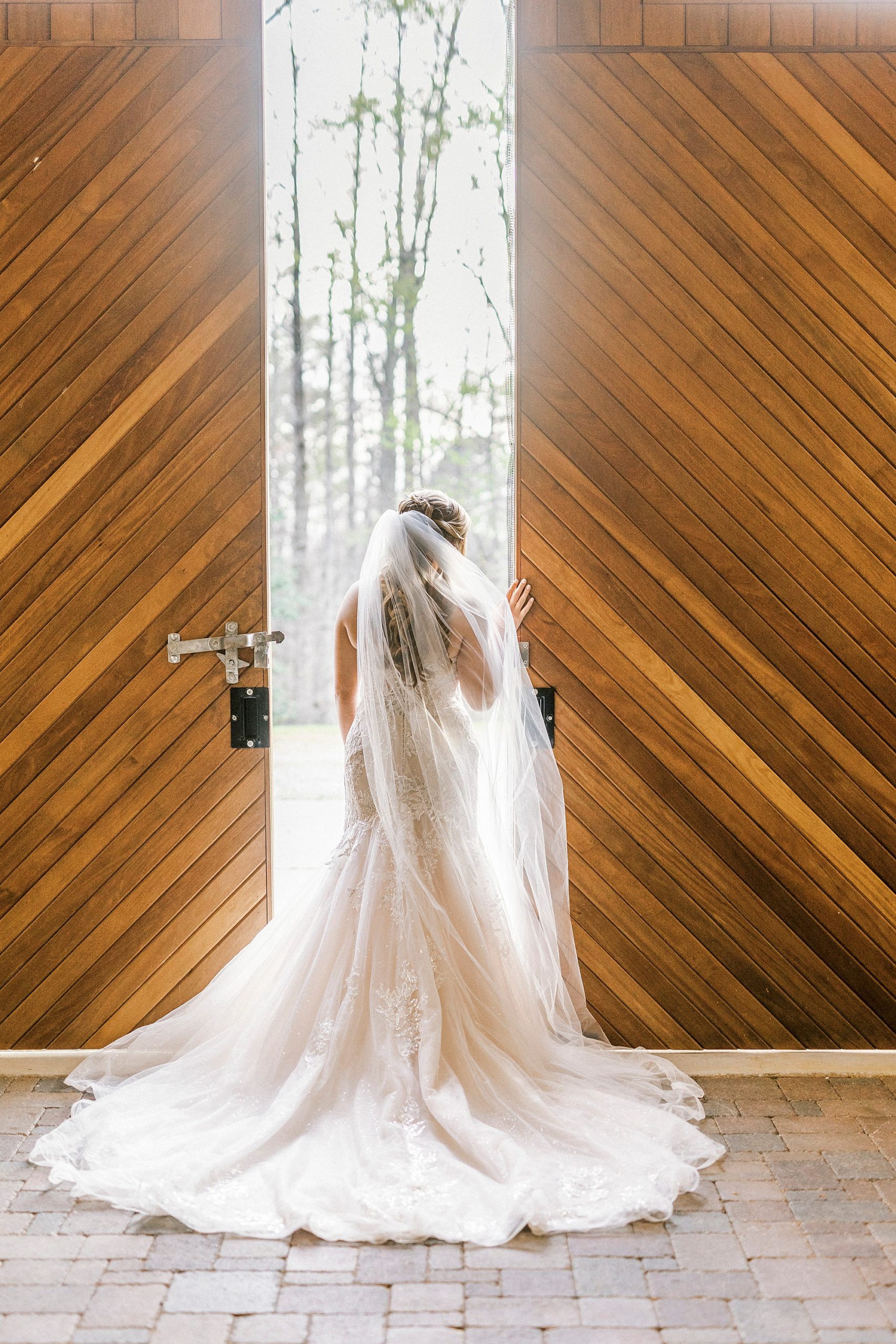 bride-to-be poses looking out wooden doors at The Stable at Riverview
