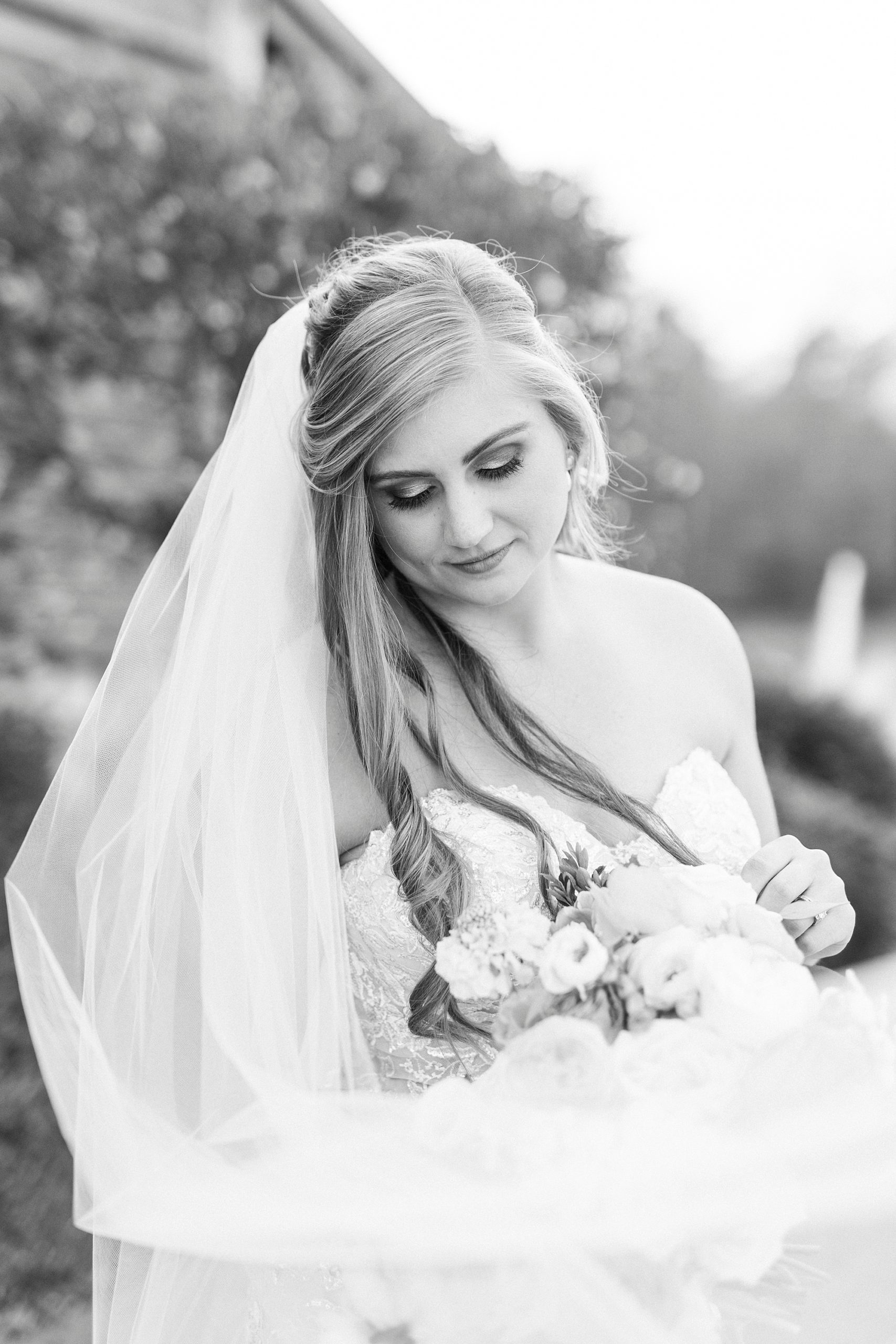 bride looks down at bouquet with veil draped around shoulders