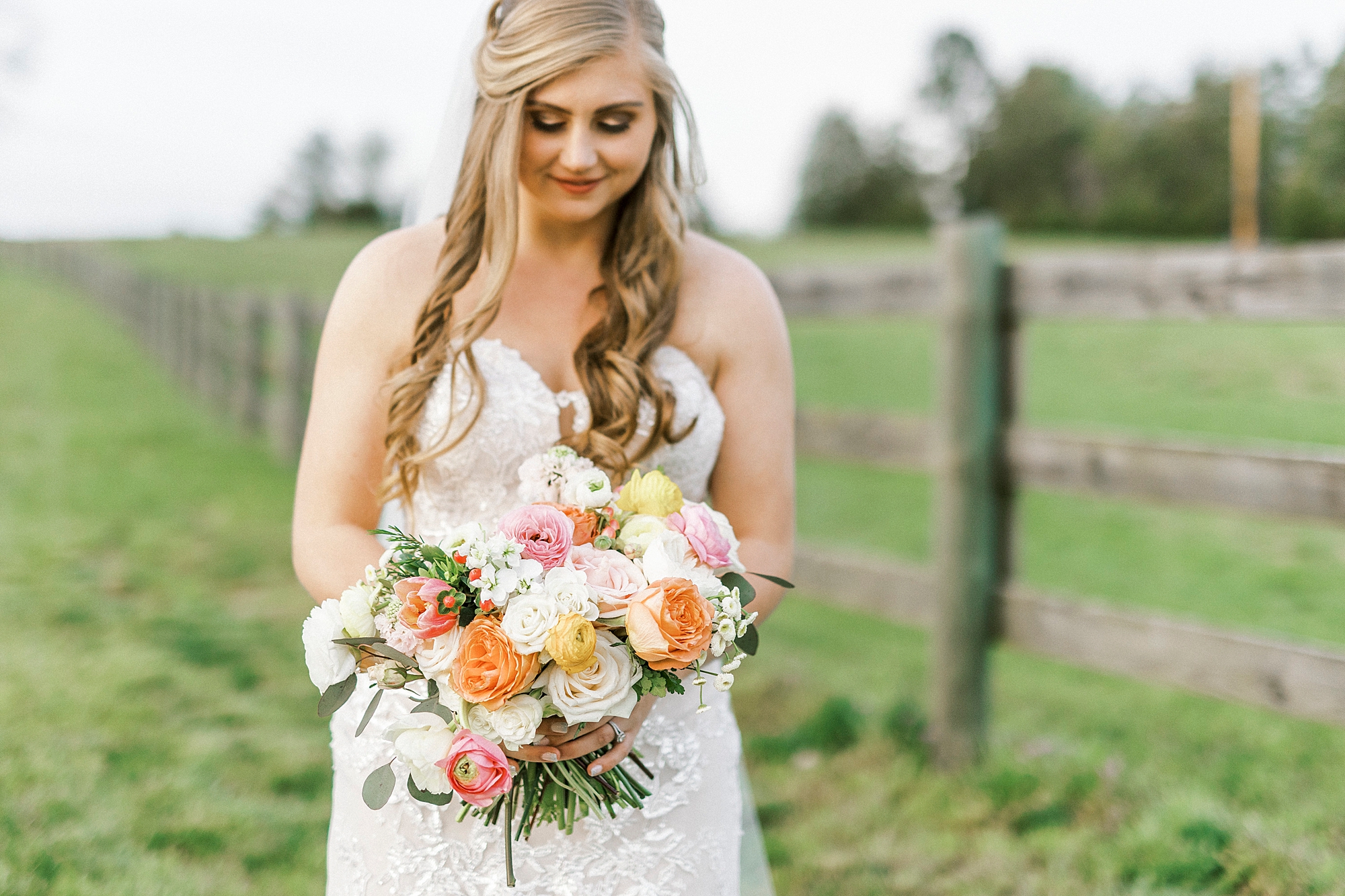 bride holds colorful bouquet of flowers by wooden fence on farm