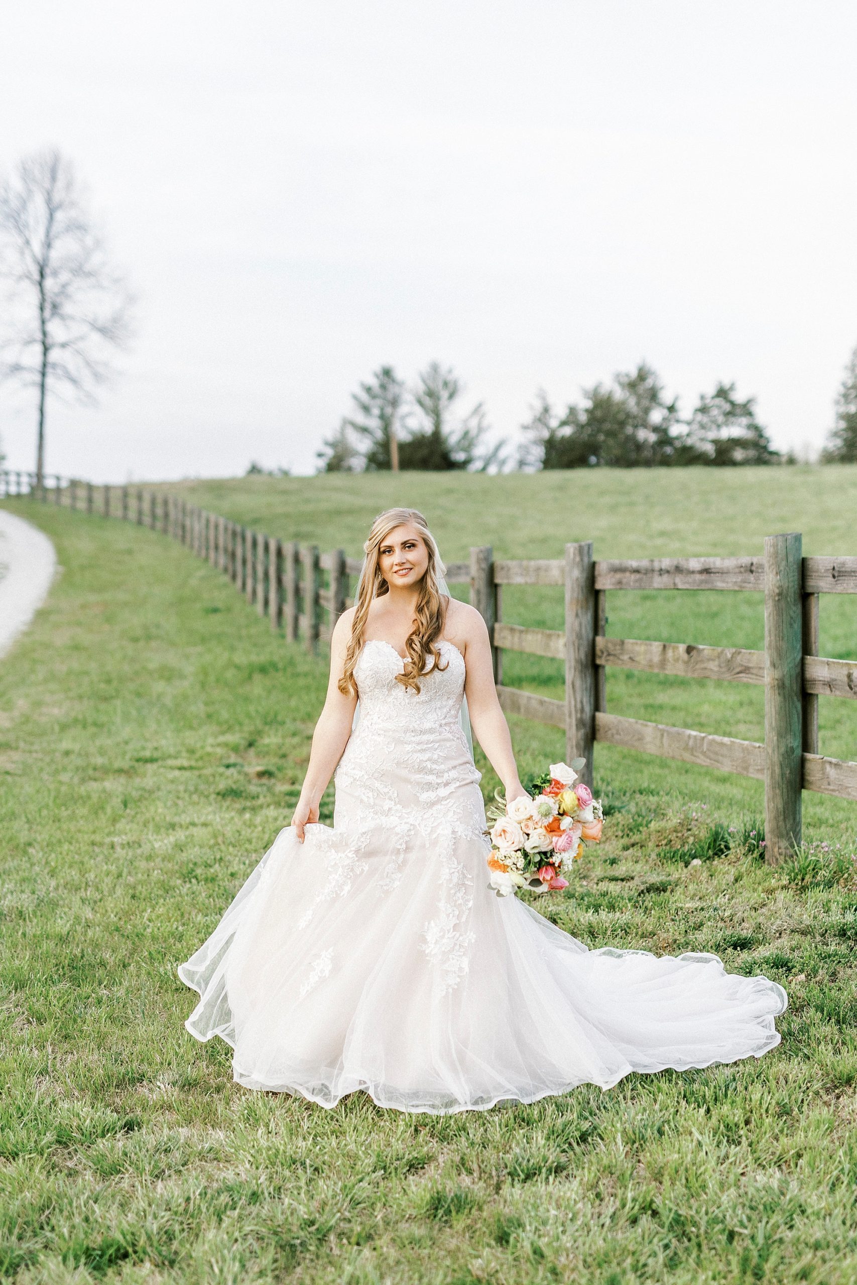 bride walks along wooden fence at The Stable at Riverview