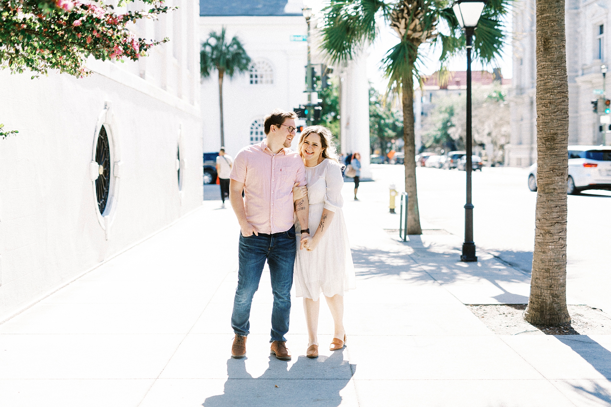 couple walks down sidewalk in downtown Charleston with palm trees around them