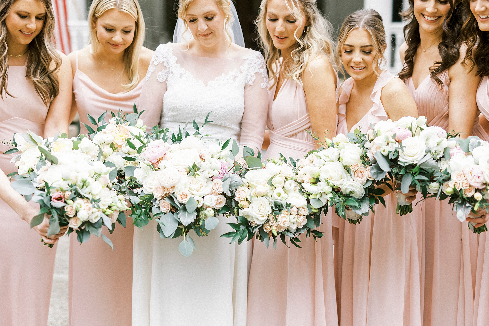 bride and bridesmaids hold bouquets of white and pink flowers