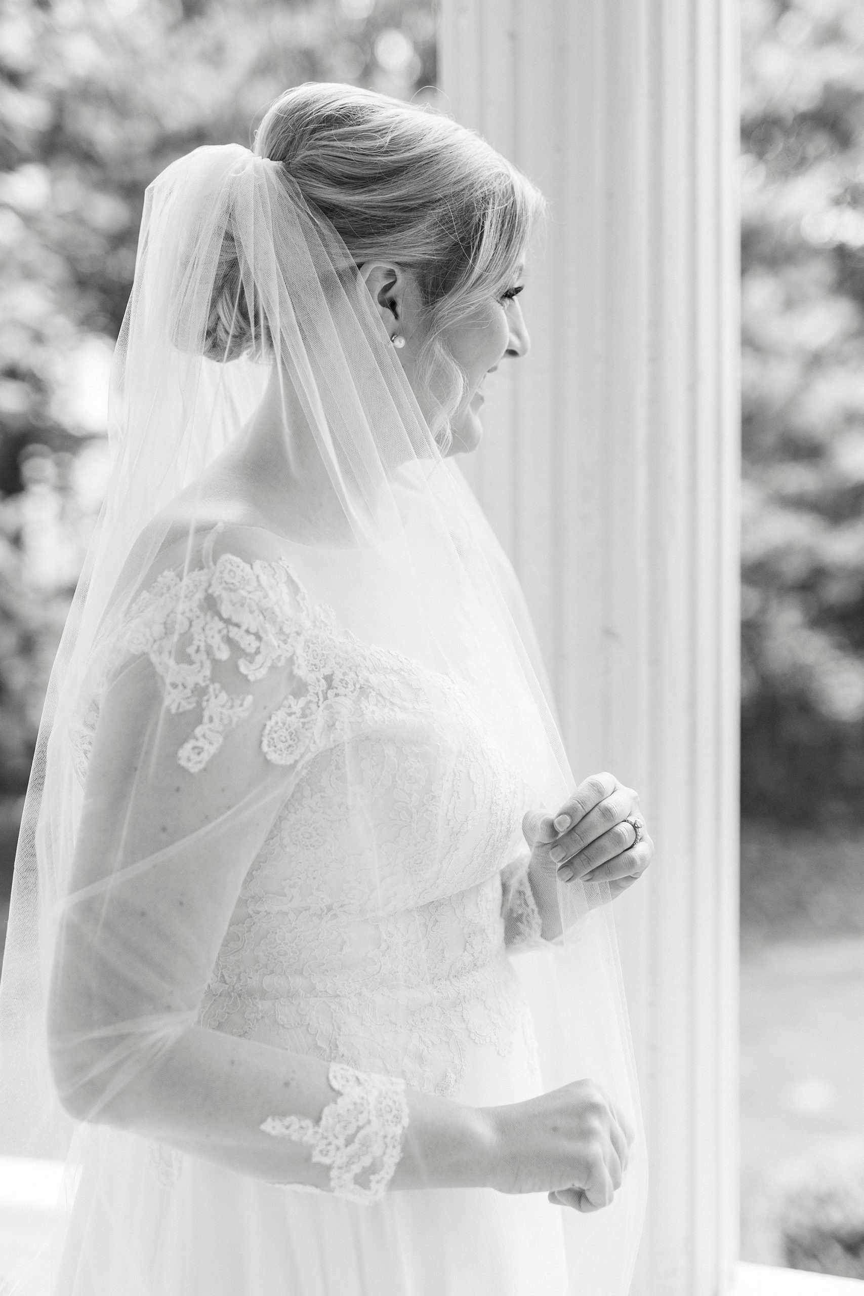bride holds edge of veil standing on porch 