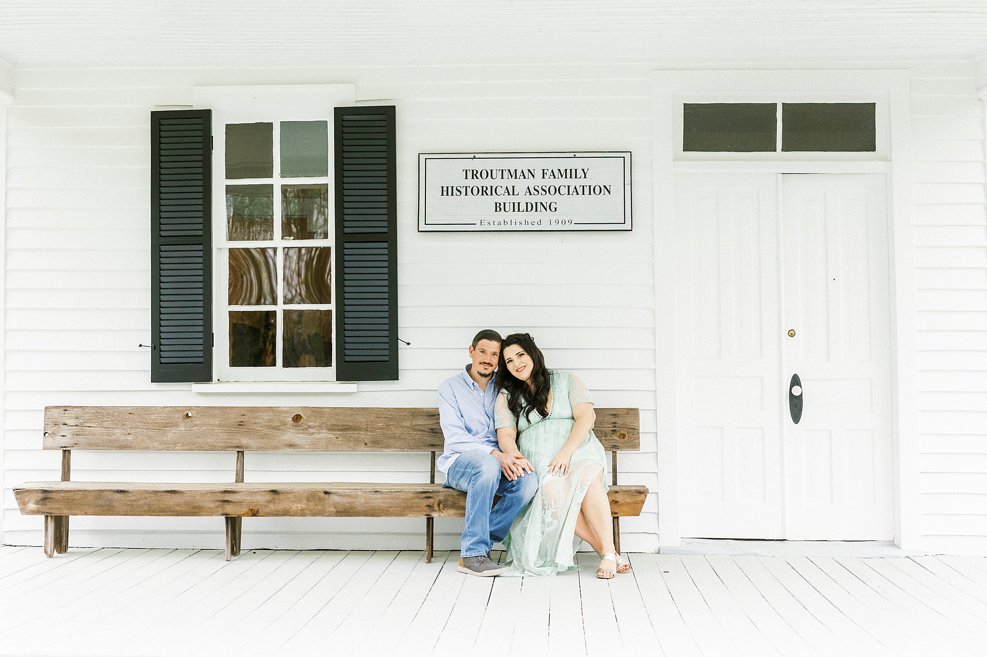 bride and groom sit on wooden bench during White Chapel engagement session