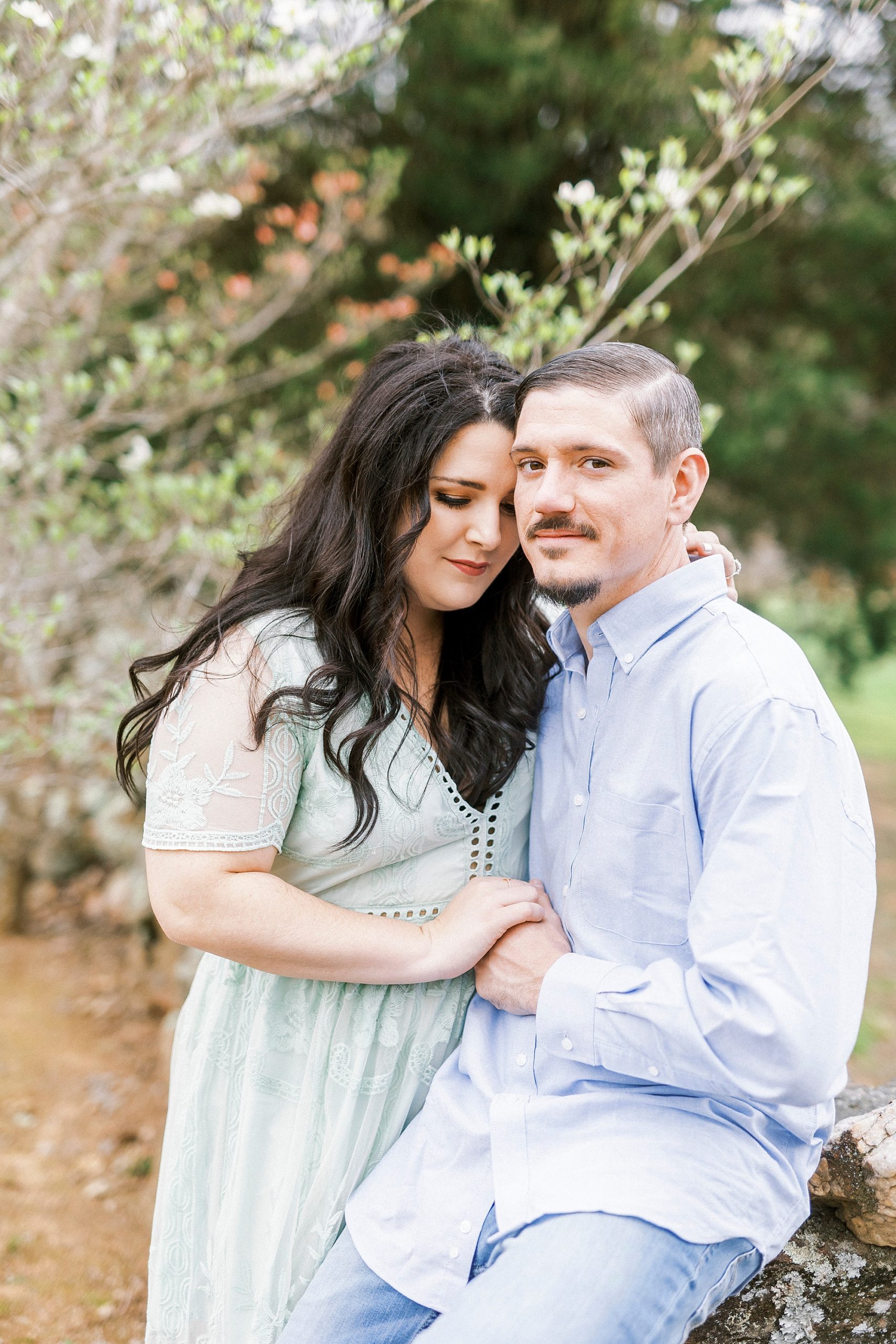 couple sits together against stone wall during white chapel engagement session