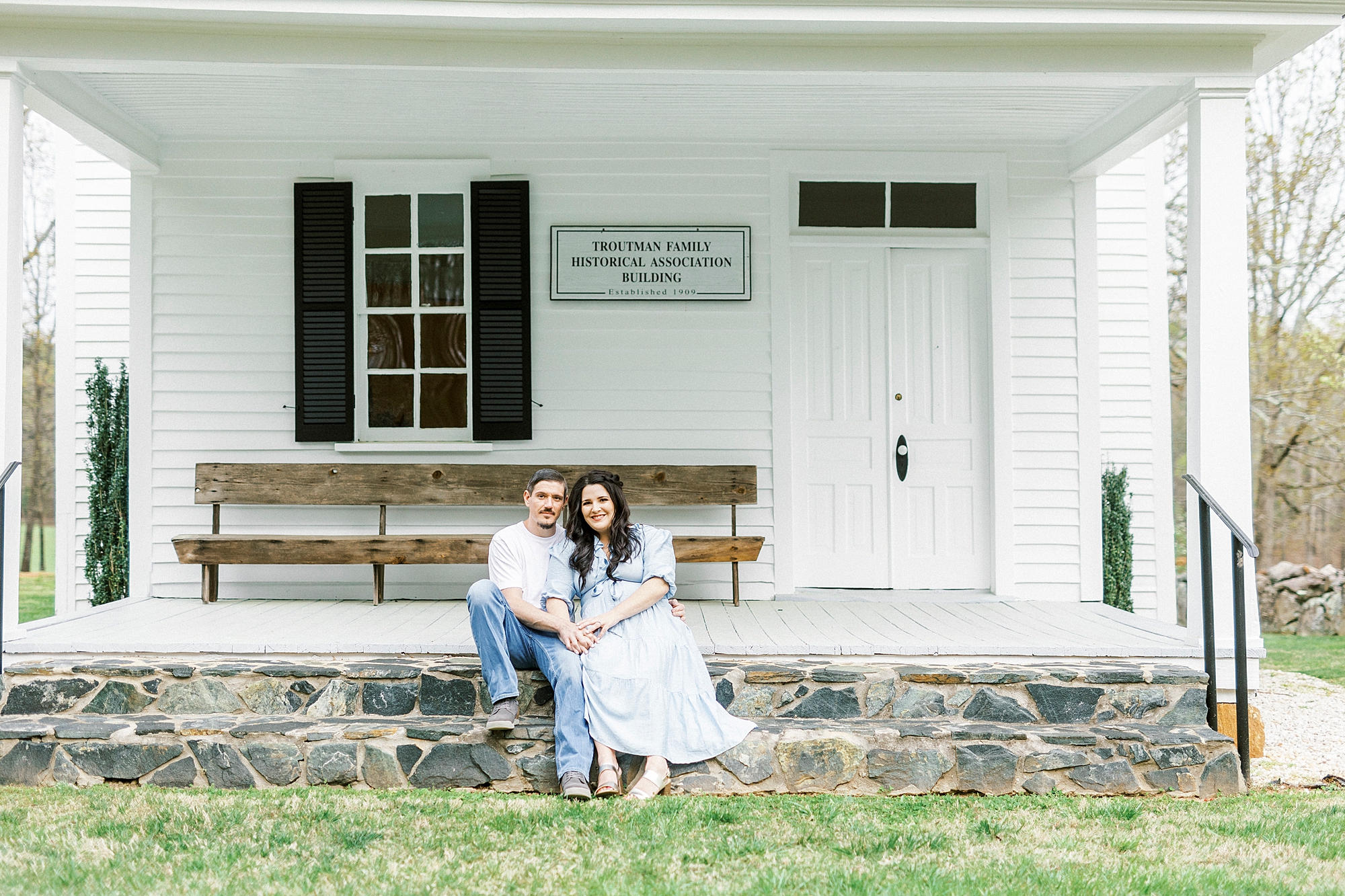couple sits on stone wall of family chapel 