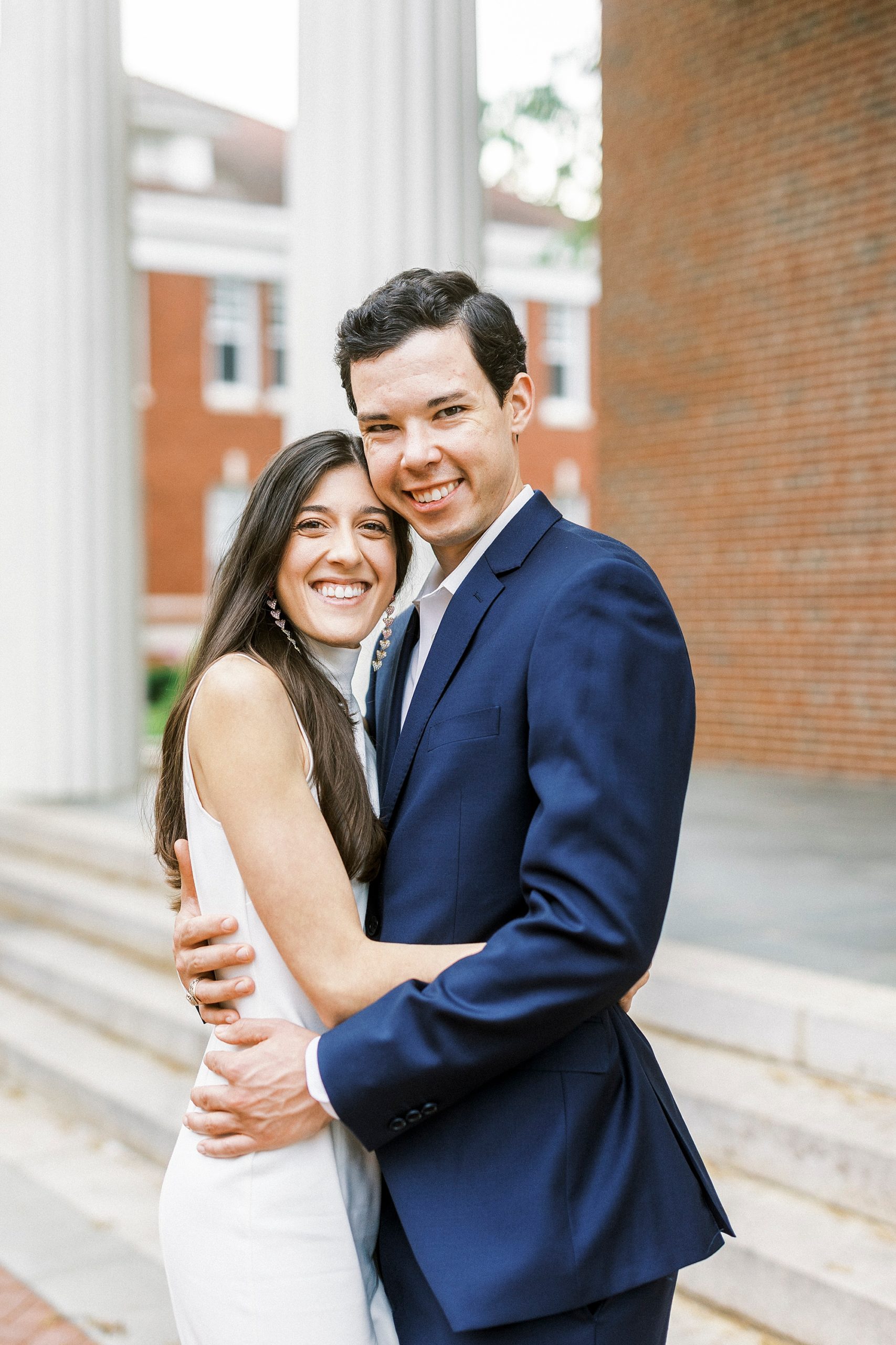 bride in white dress hugs groom in navy suit during engagement photos at Queens University