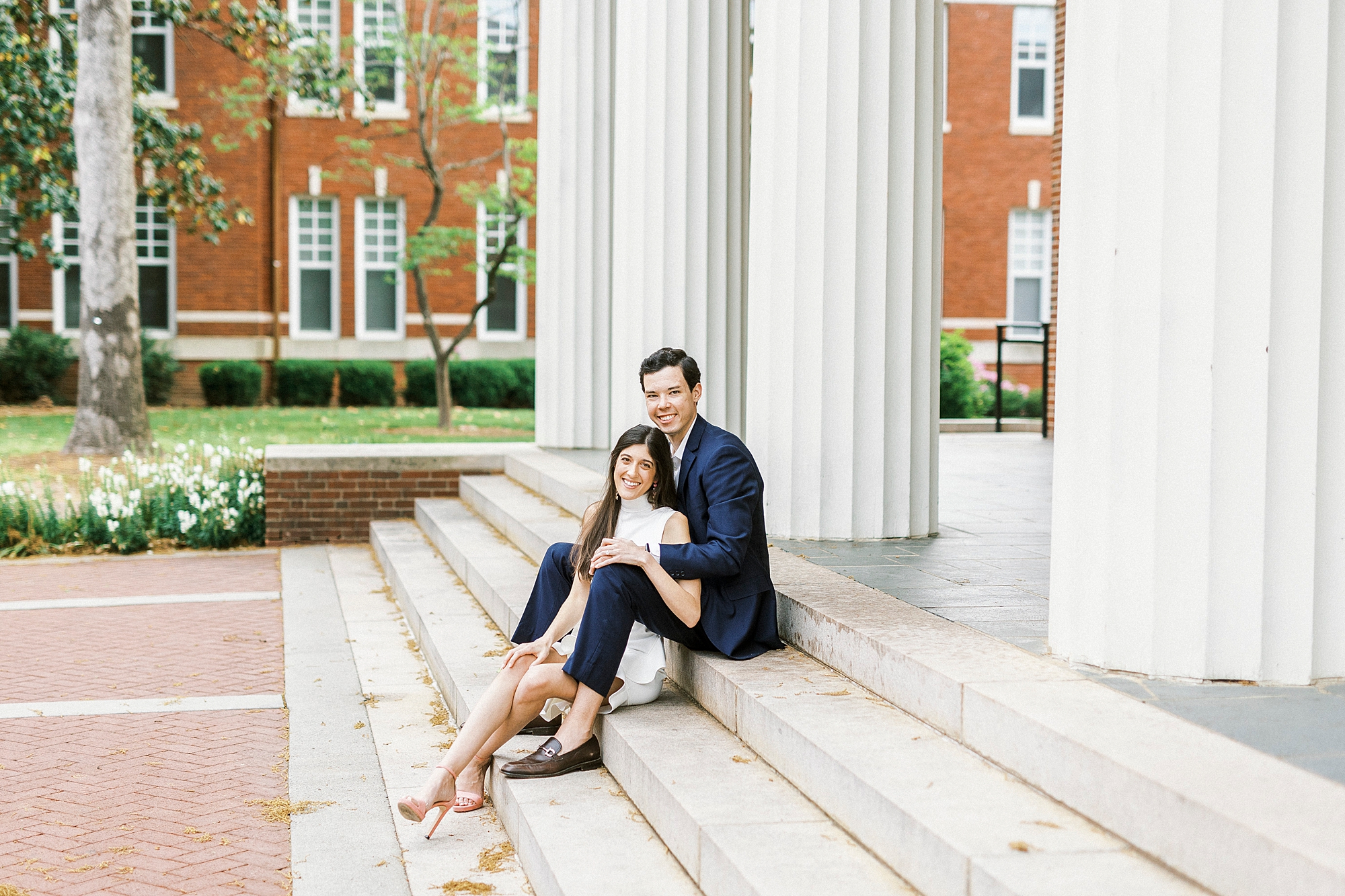 engaged couple sits on steps of building at Queens University