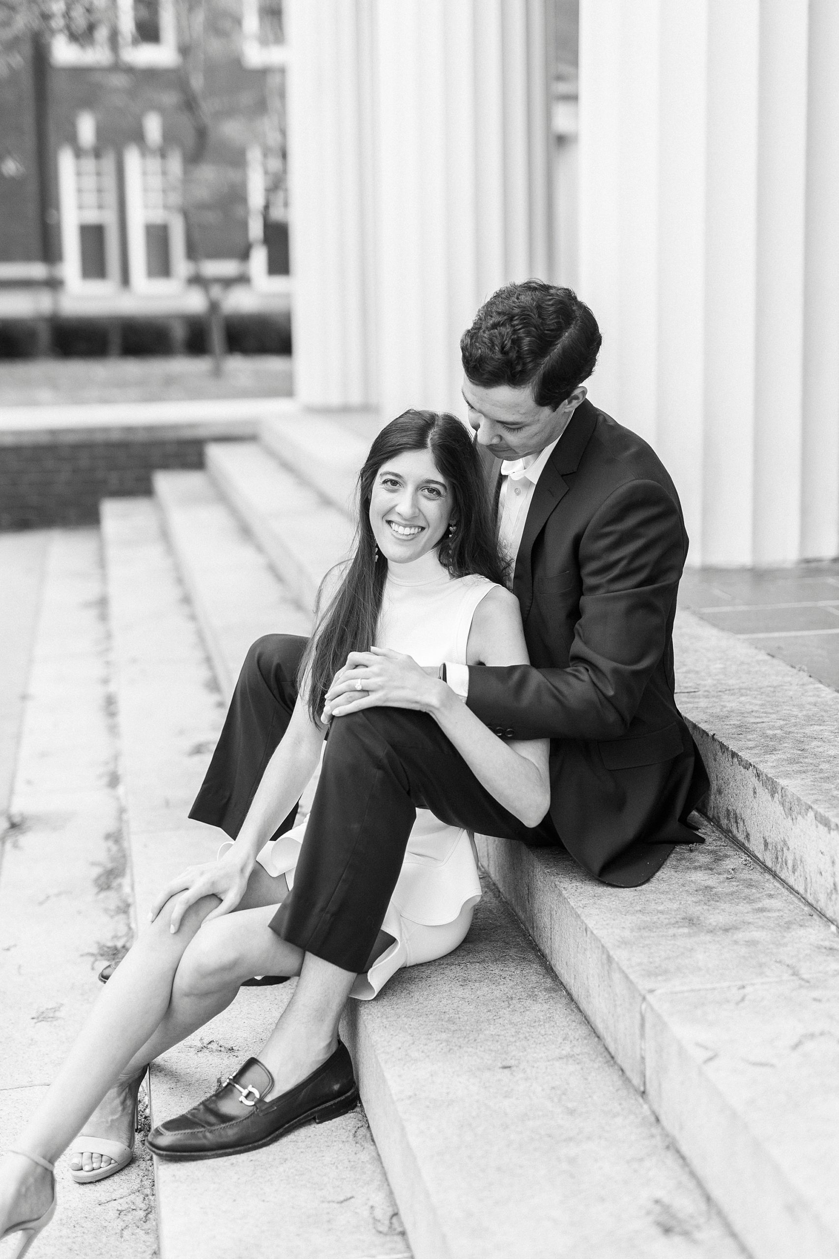 groom sits behind bride on steps during Queens University engagement session