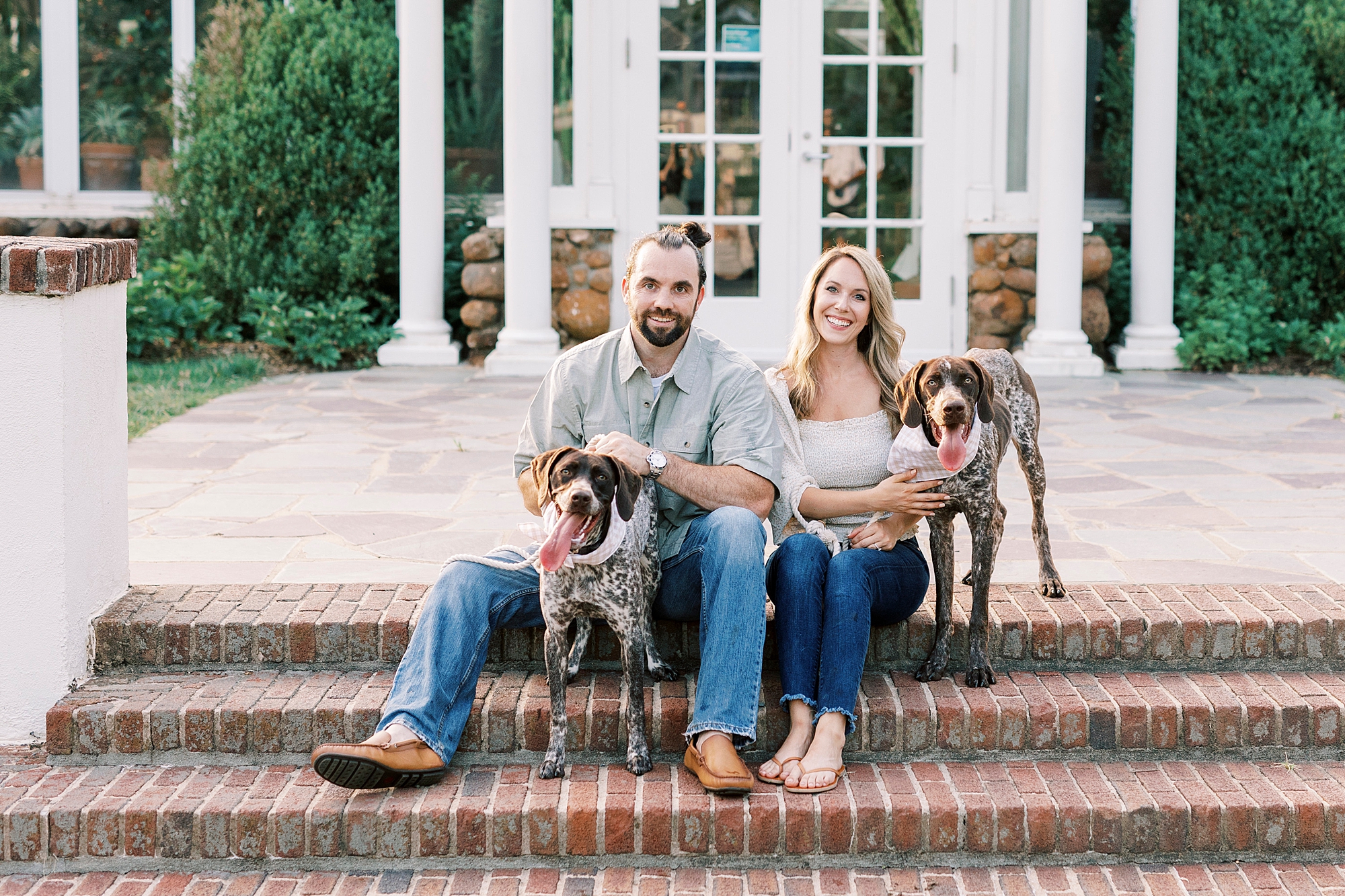 couple sits on brick steps at Reynolda Gardens with GSP dogs