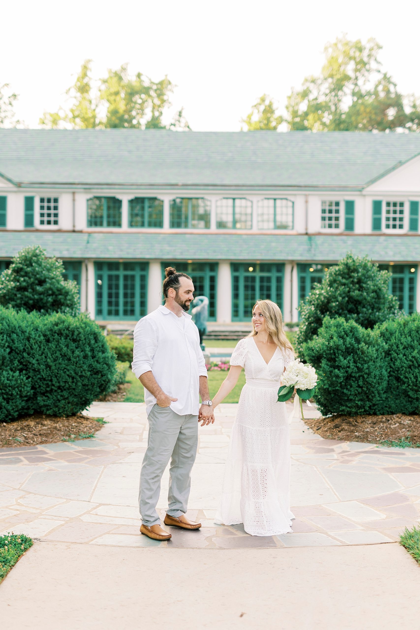 engaged couple walks down pathway by house at Reynolda Gardens