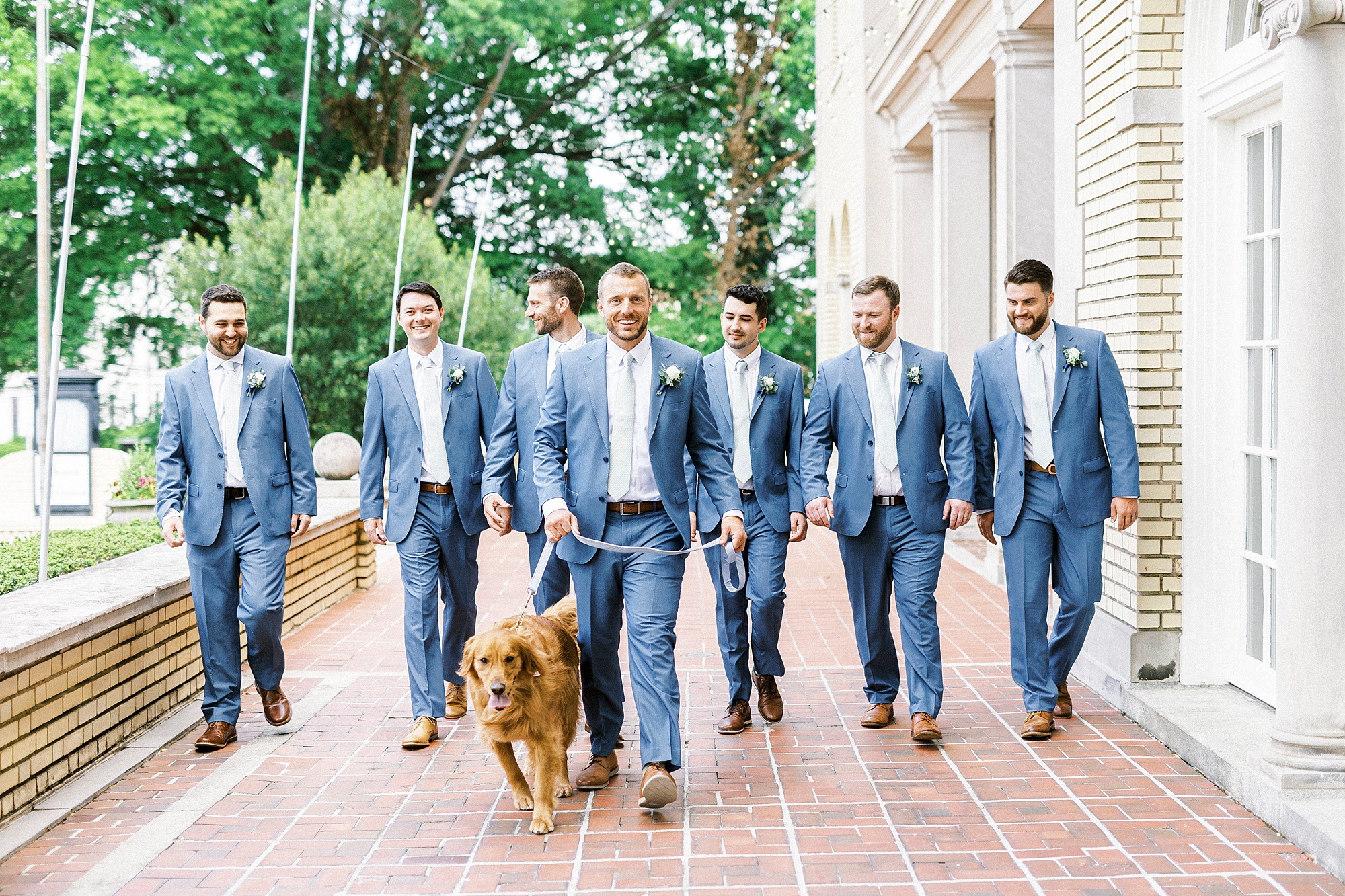groom walks with groomsmen in navy suits with golden retriever on patio at Separk Mansion