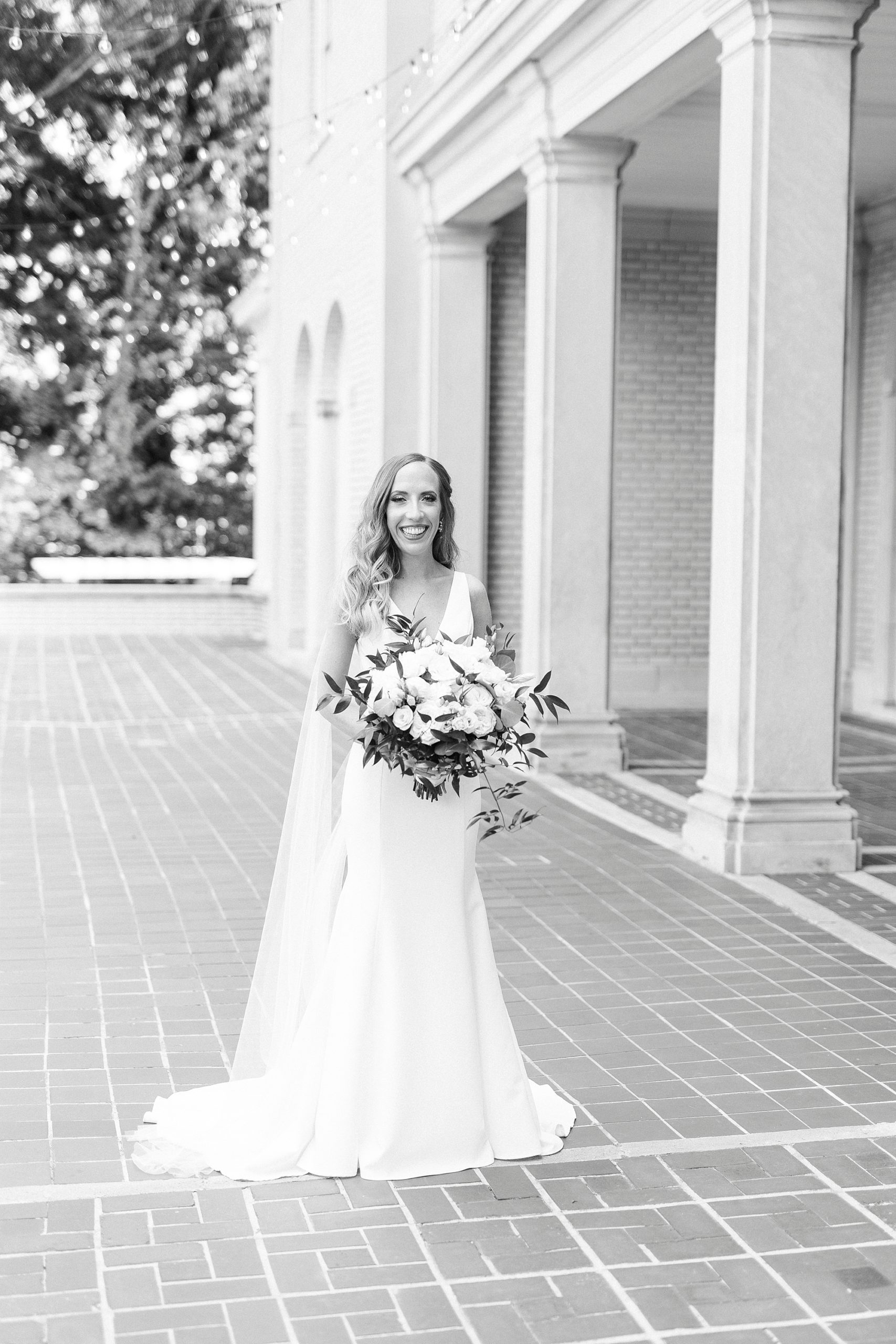 bride stands outside Separk Mansion holding bouquet with wings on dress