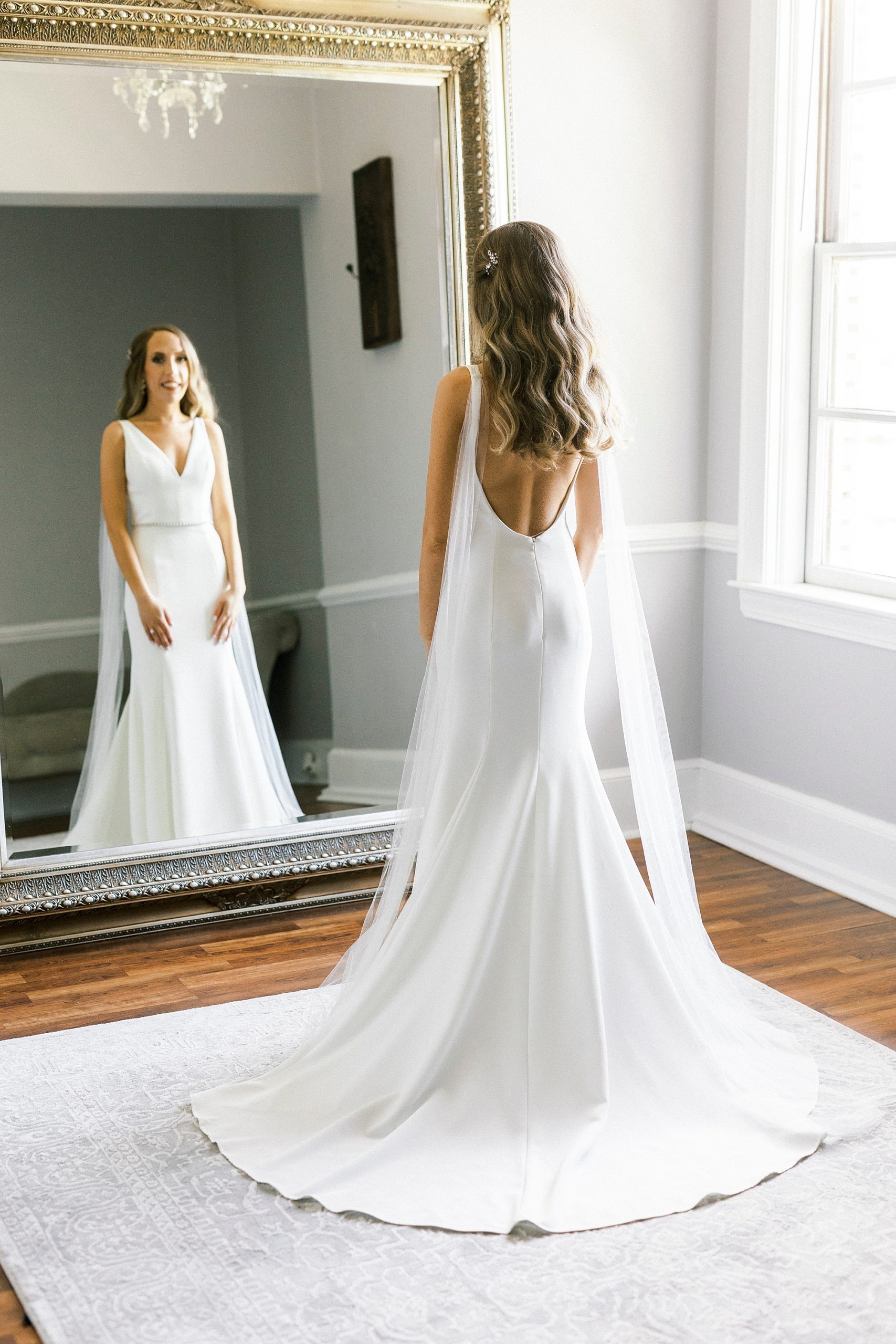 bride looks at herself in gold mirror at Separk Mansion with sleek wedding gown