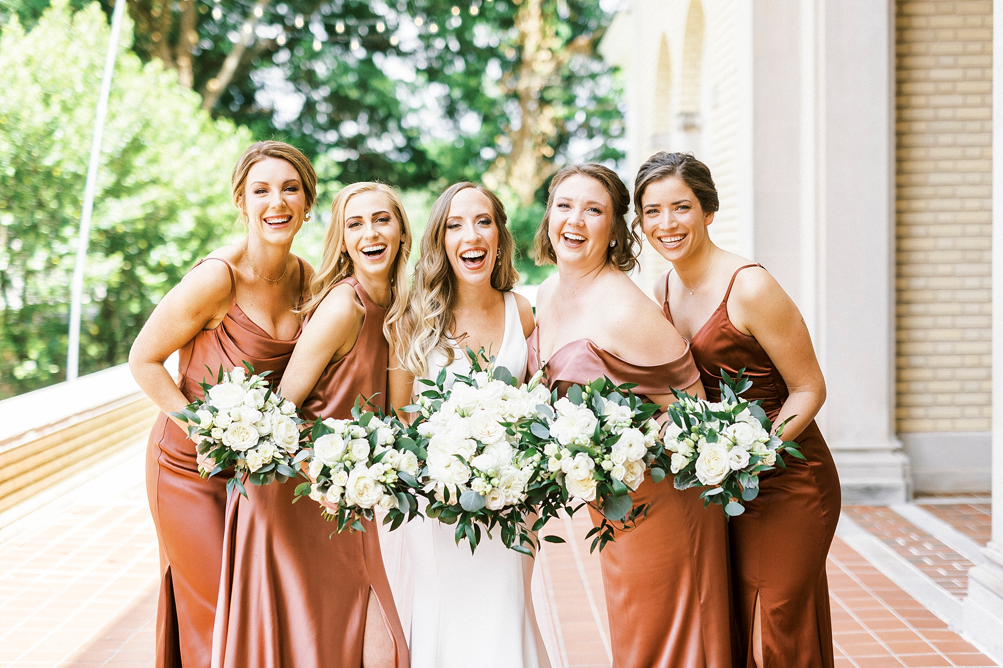 bride and bridesmaids hold white bouquets in copper gowns on patio at Separk Mansion