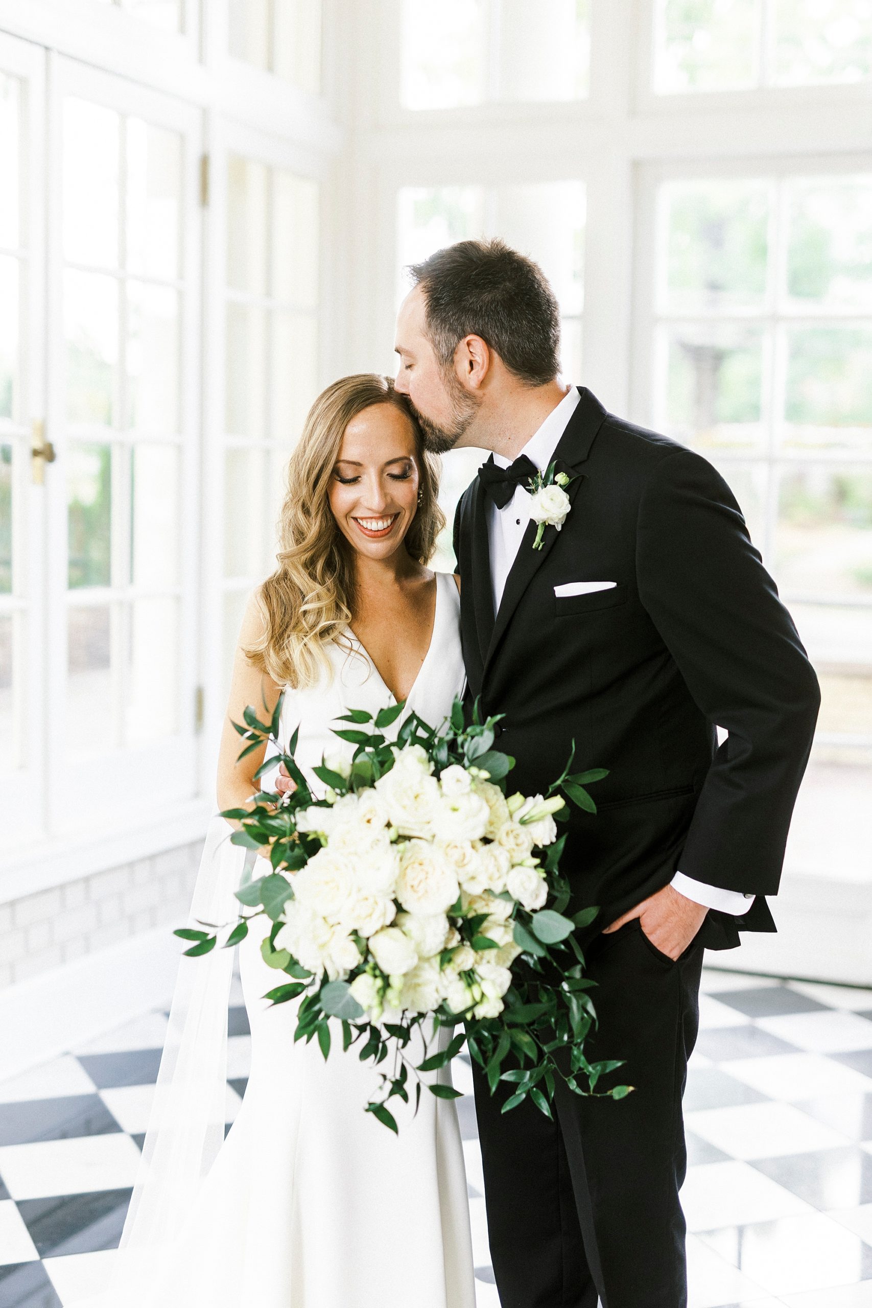 groom kisses bride's head during Separk Mansion wedding portraits in sunroom