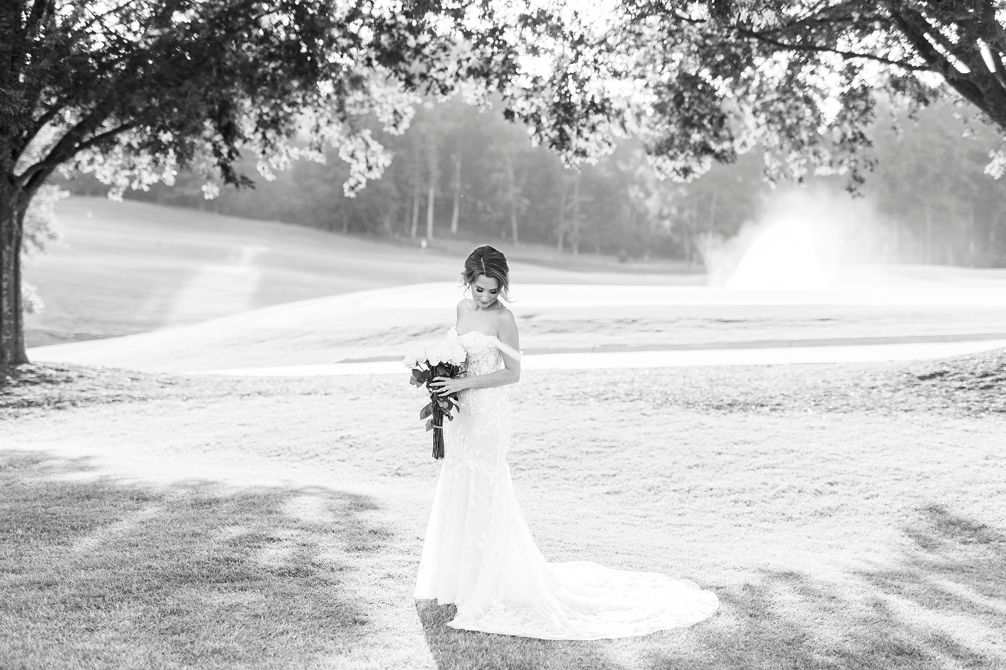 bride holds bouquet under trees by the water at golf club