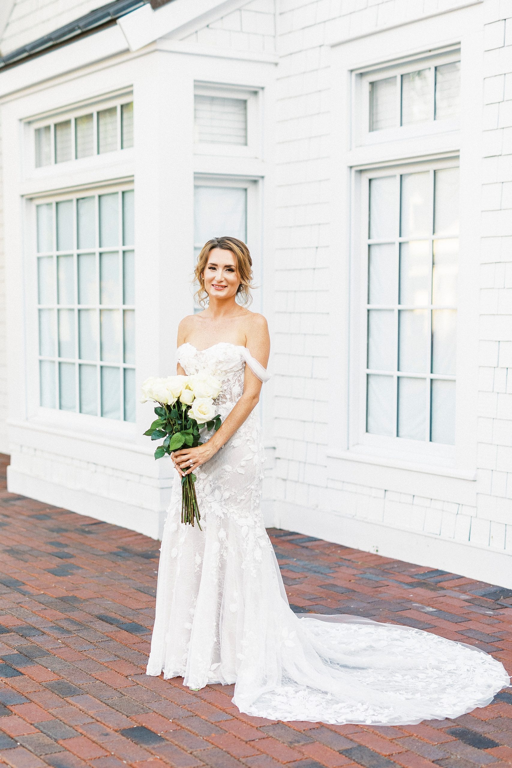 bride stands holding white bouquet by white walls of Trump National Golf Club