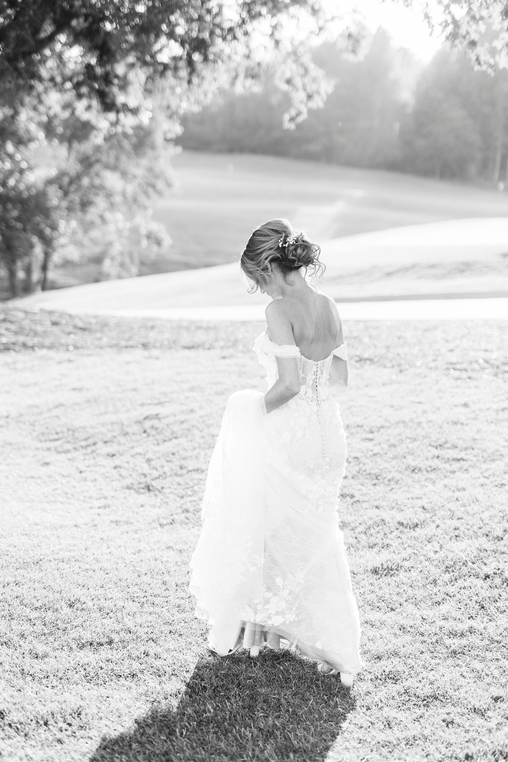 bride walks through golf course holding wedding gown